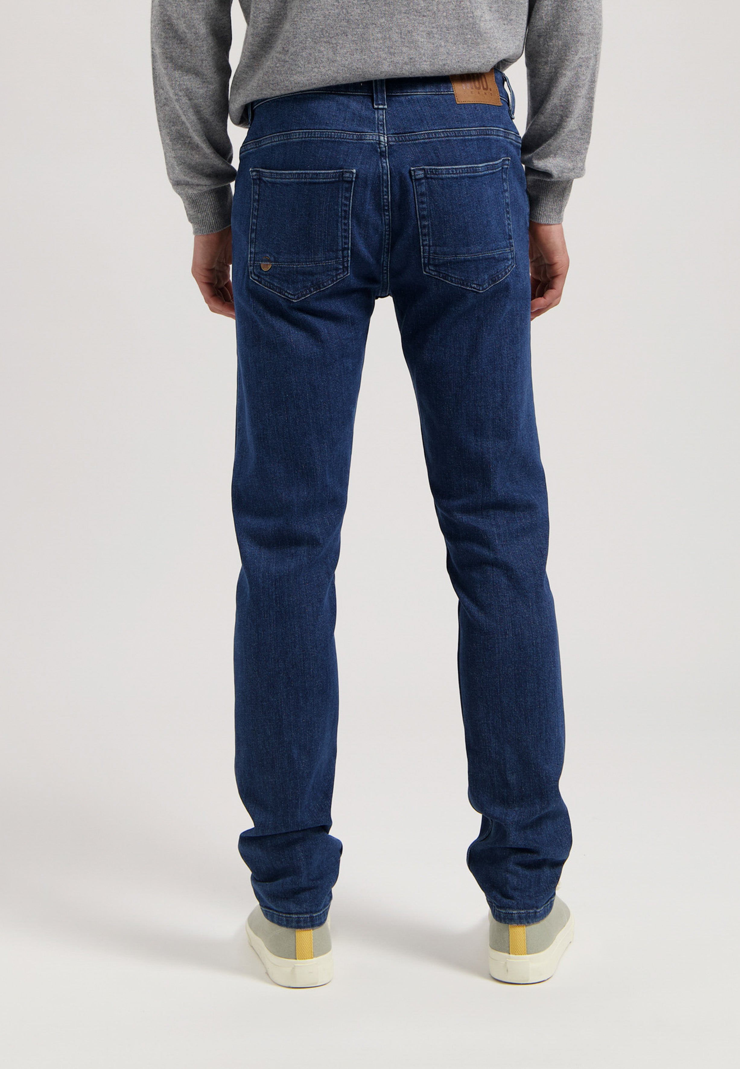 Sustainable MUD Jeans made from organic cotton, featuring classic blue denim, paired with a gray sweater and white sneakers.