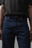 Sustainable MUD Jeans in black denim, featuring an ethical design, paired with a soft gray sweater and white sneakers.