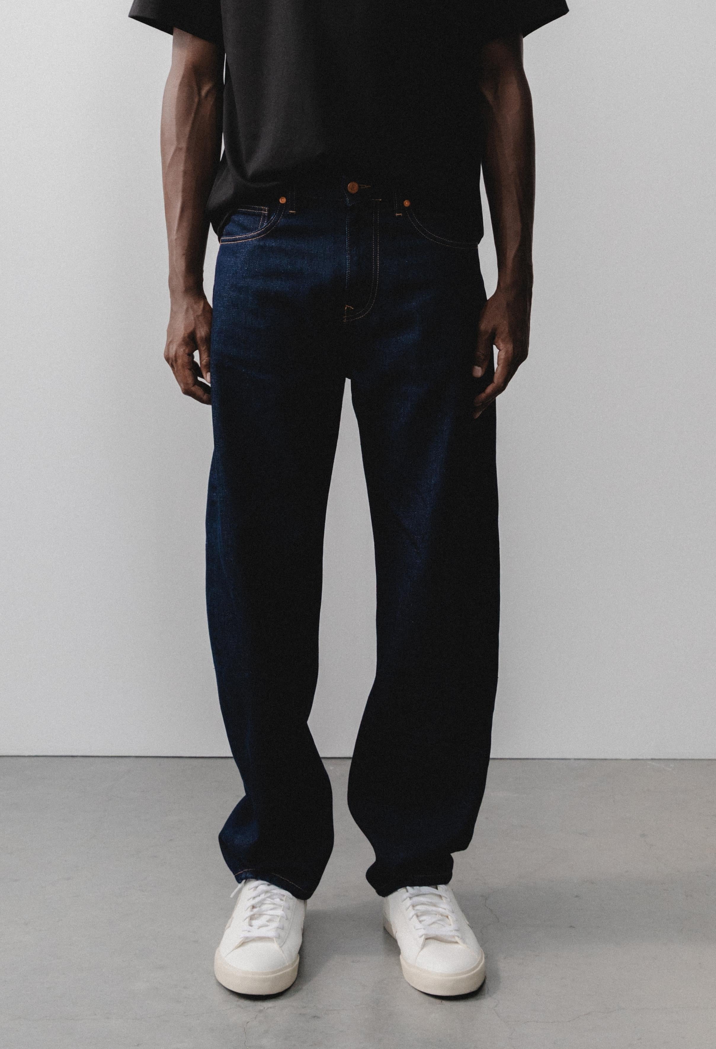 Sustainable MUD Jeans with a modern fit in deep black denim, paired with a casual gray sweater and white sneakers.