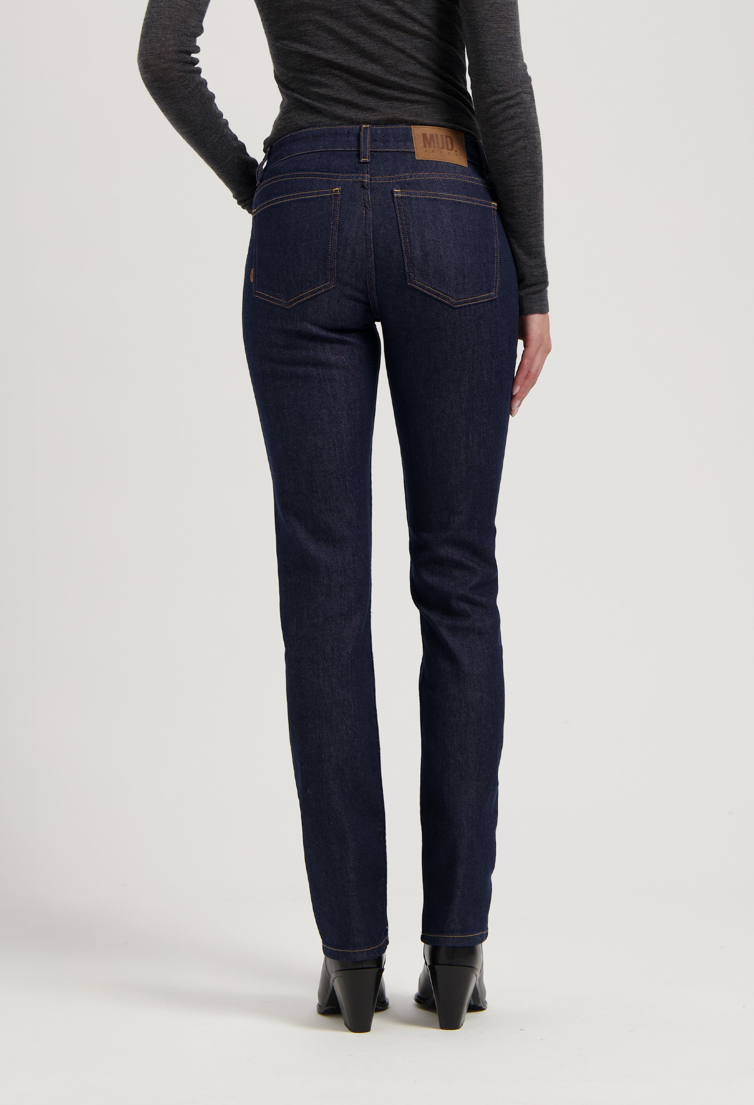 Dark blue, slim-fit MUD Jeans made from organic cotton, shown from the back, paired with a long-sleeve gray top and black boots.