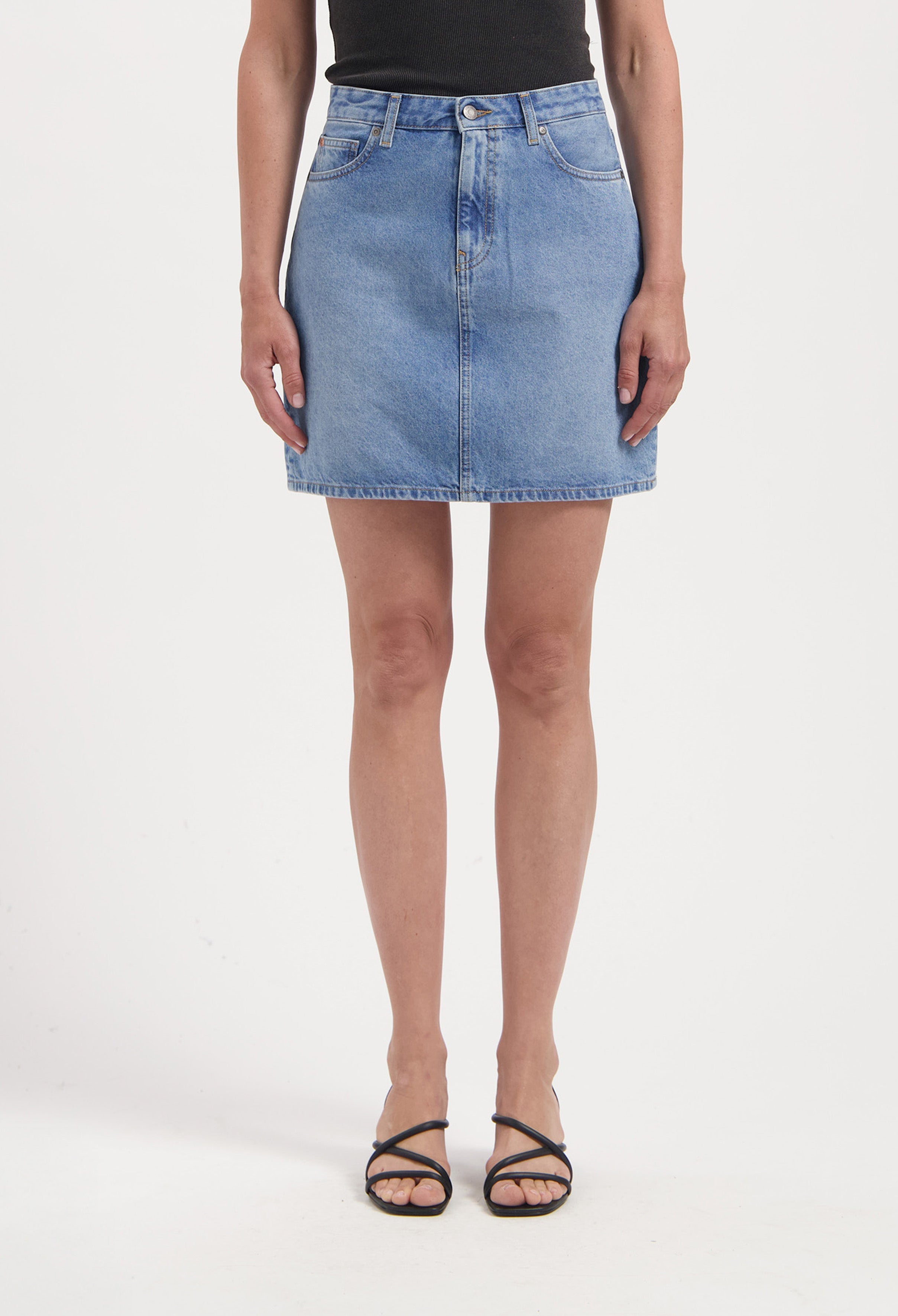 Light blue denim skirt in classic A-line style, paired with a black sleeveless top, worn with strappy black sandals.