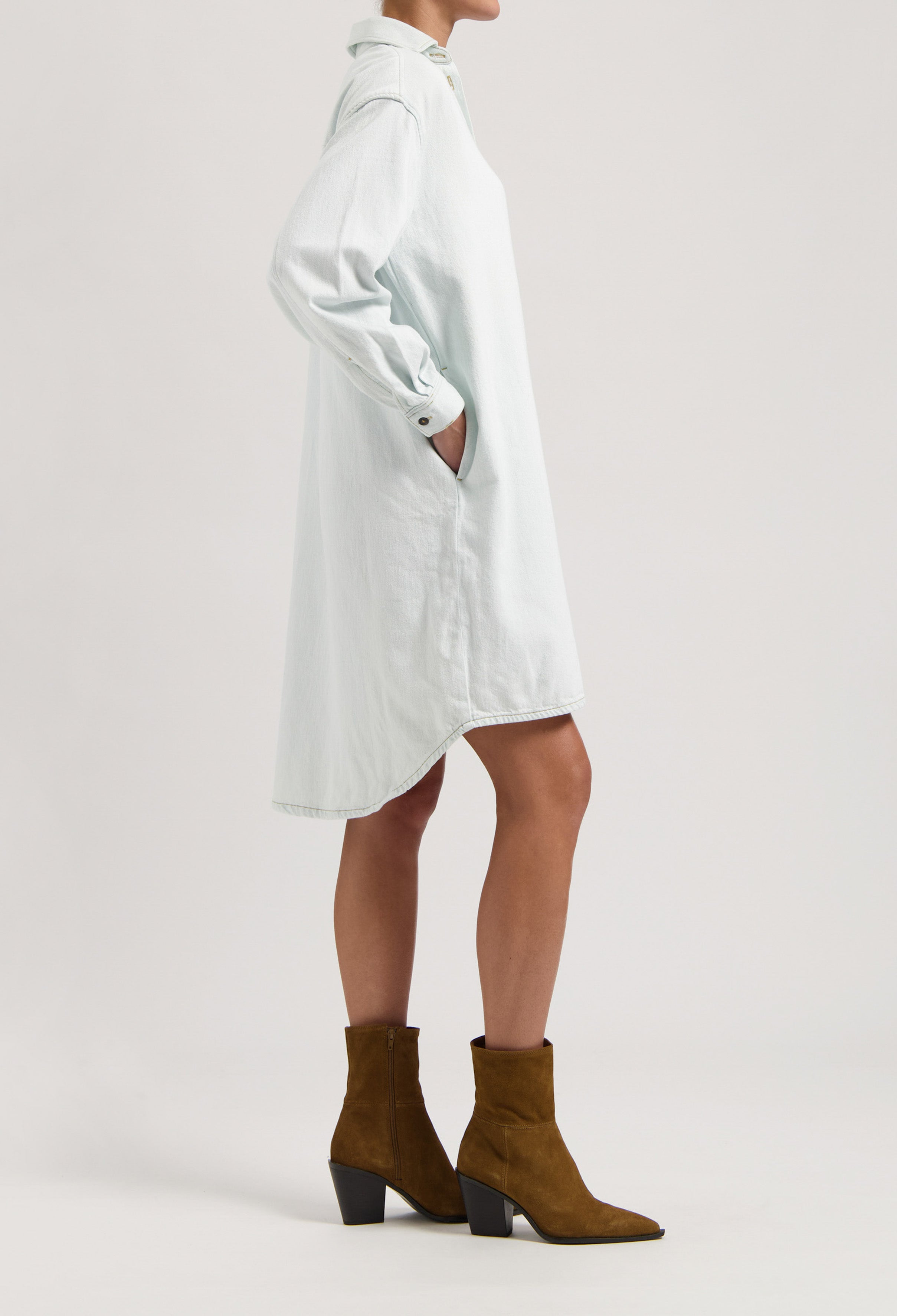 Minimalist light blue shirt dress with long sleeves and curved hem, paired with stylish brown suede ankle boots.