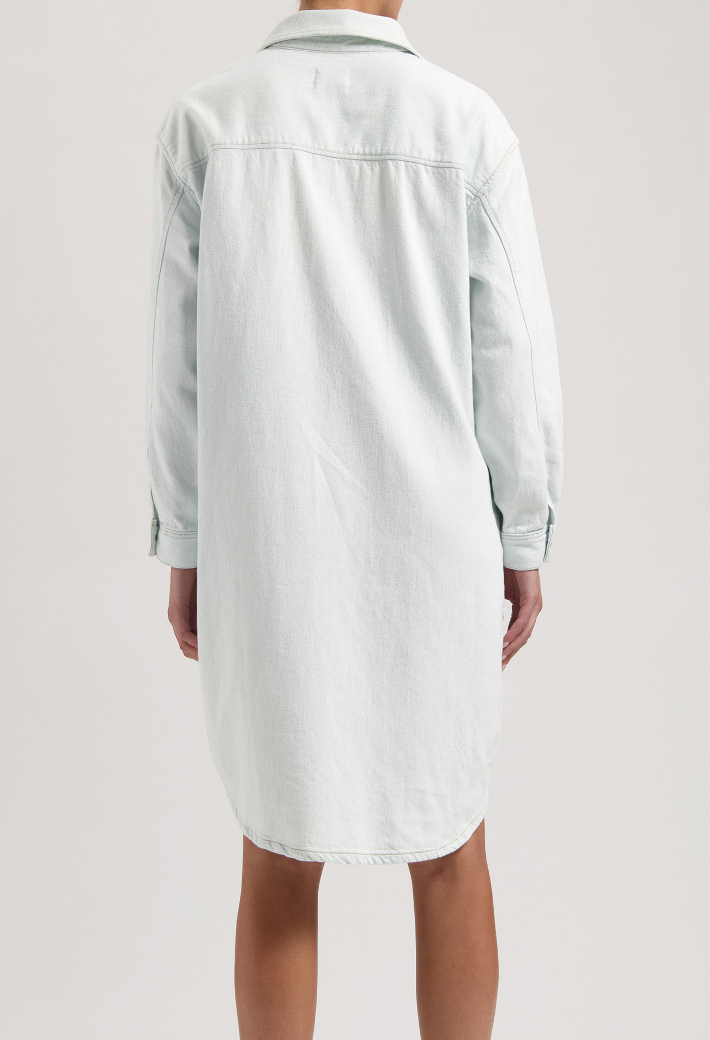 Back view of a light blue denim shirt dress showing a relaxed fit with long sleeves and classic collar design.
