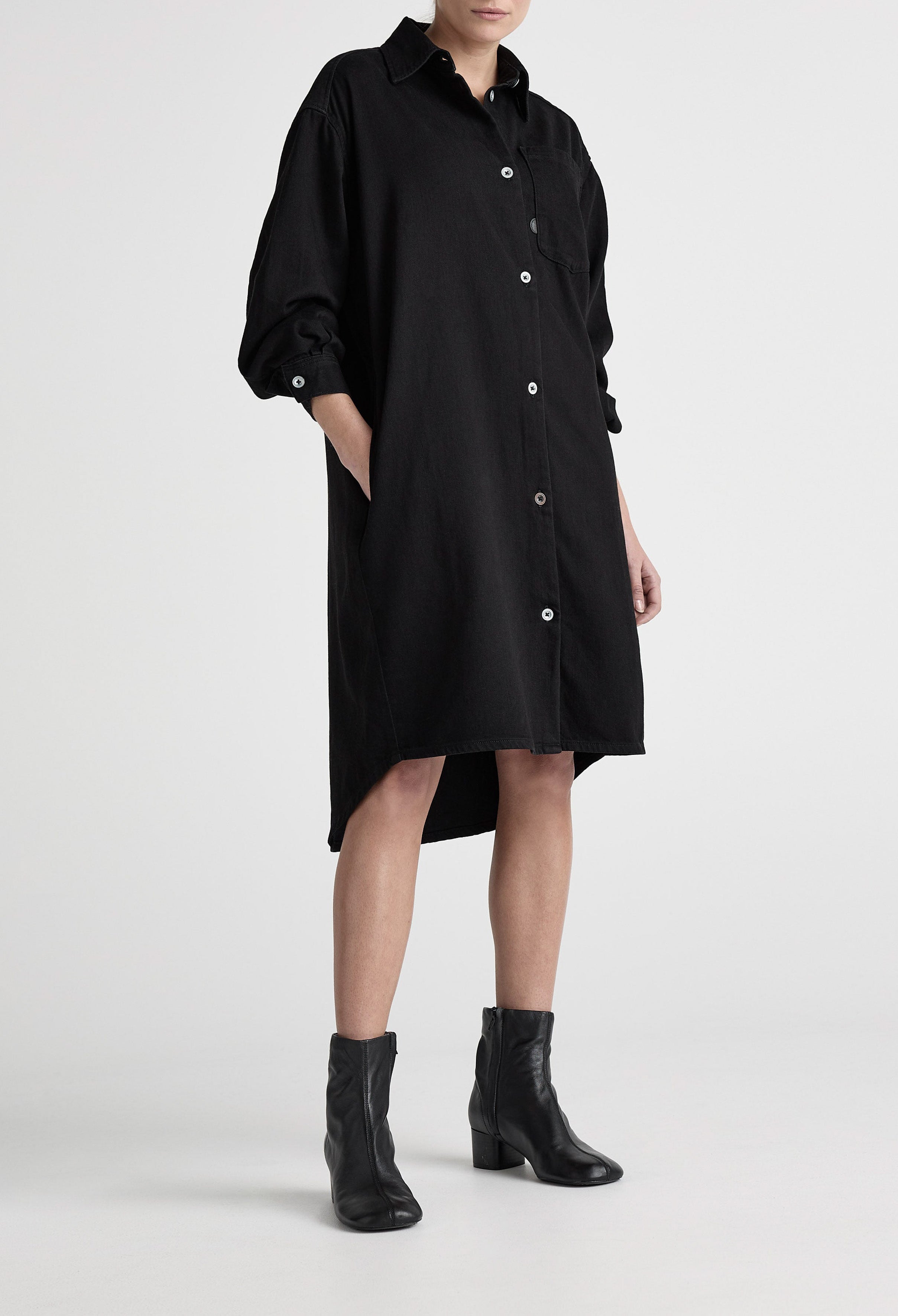 Black denim shirt dress with button-down front, featuring long sleeves and knee-length hem, paired with black ankle boots.