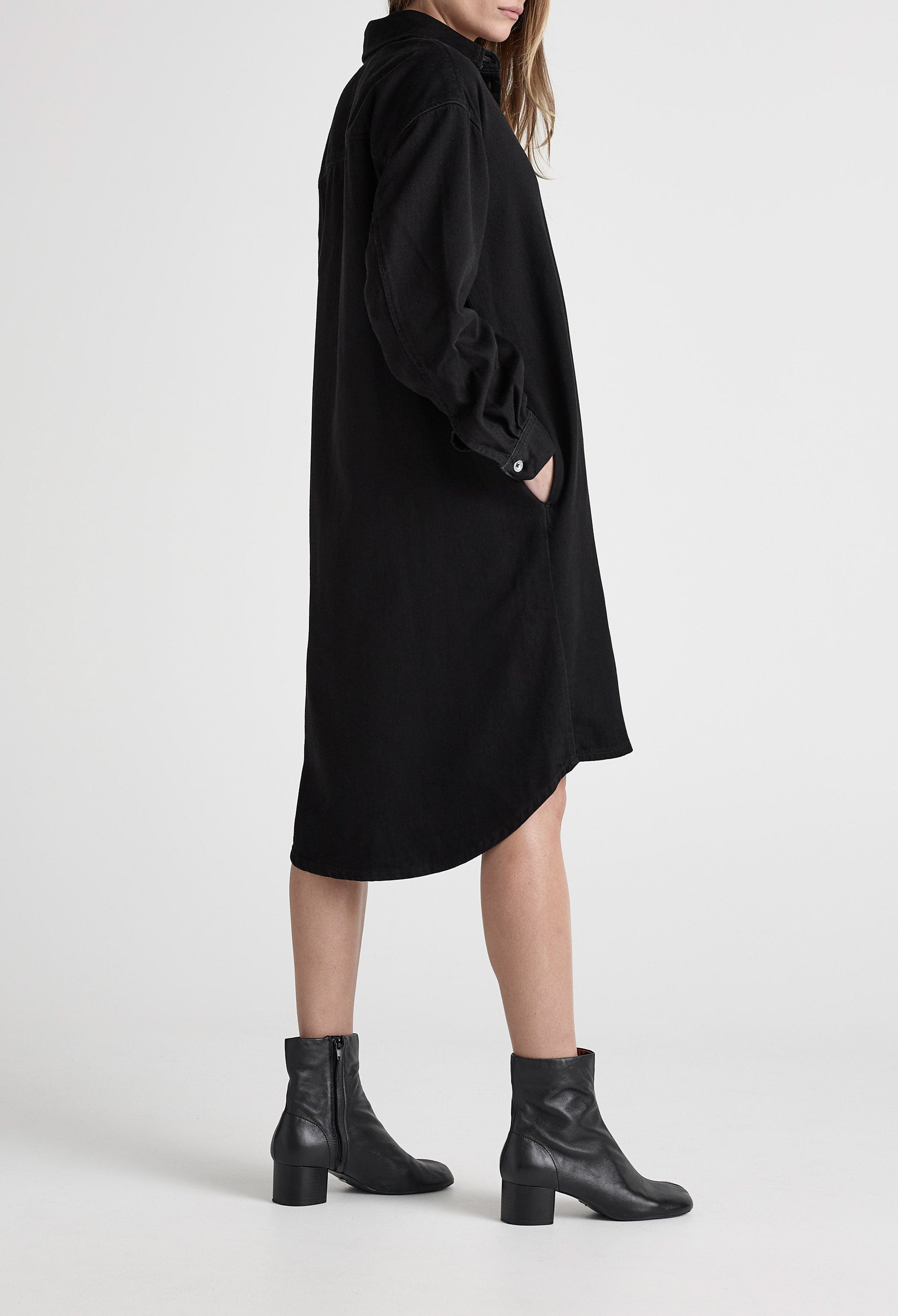 Black long-sleeve denim shirt dress with side pockets, paired with black mid-calf leather boots on a neutral background.