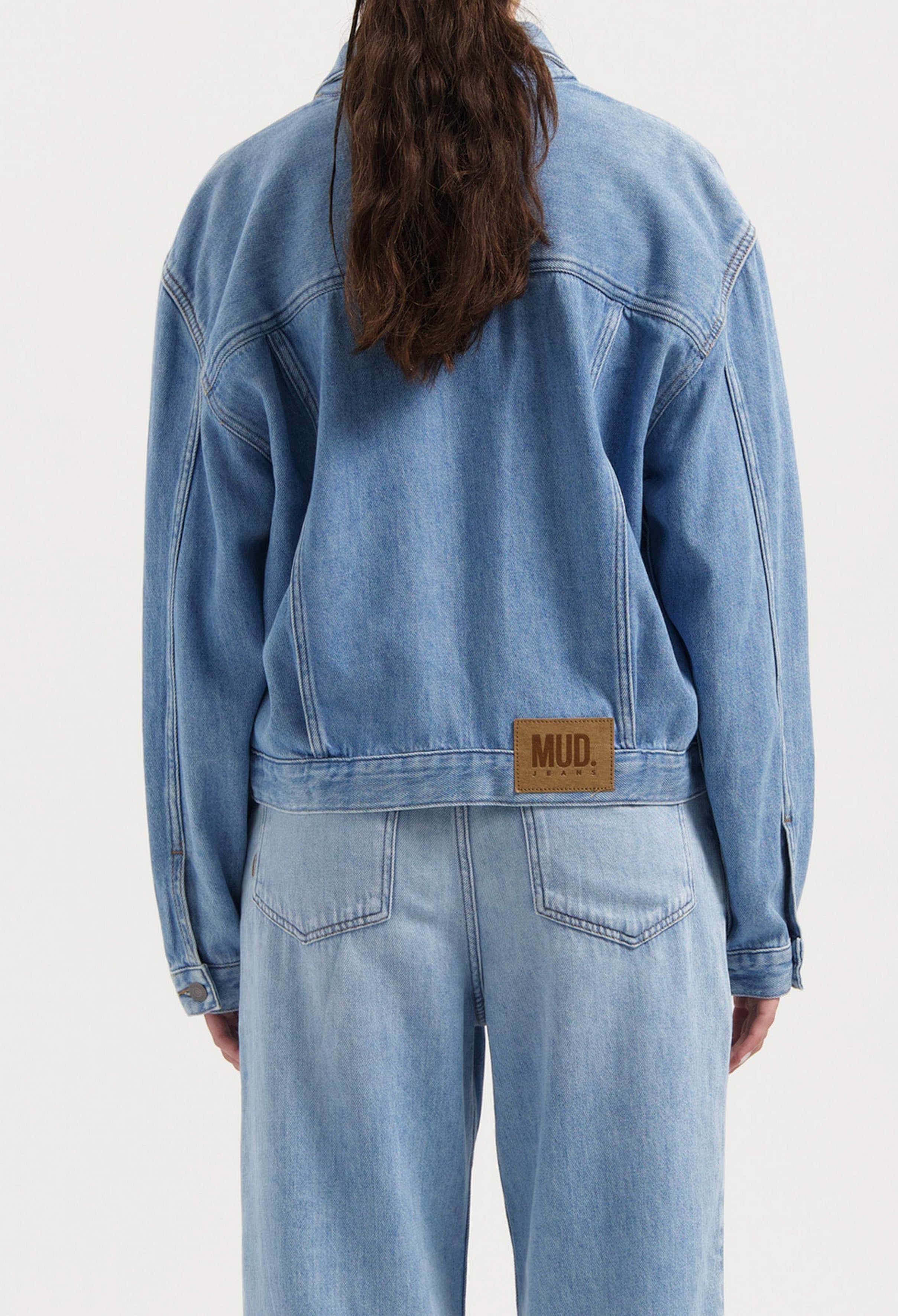 Back view of a light blue denim jacket and jeans with a sustainable MUD Jeans label, showcasing casual eco-friendly fashion.