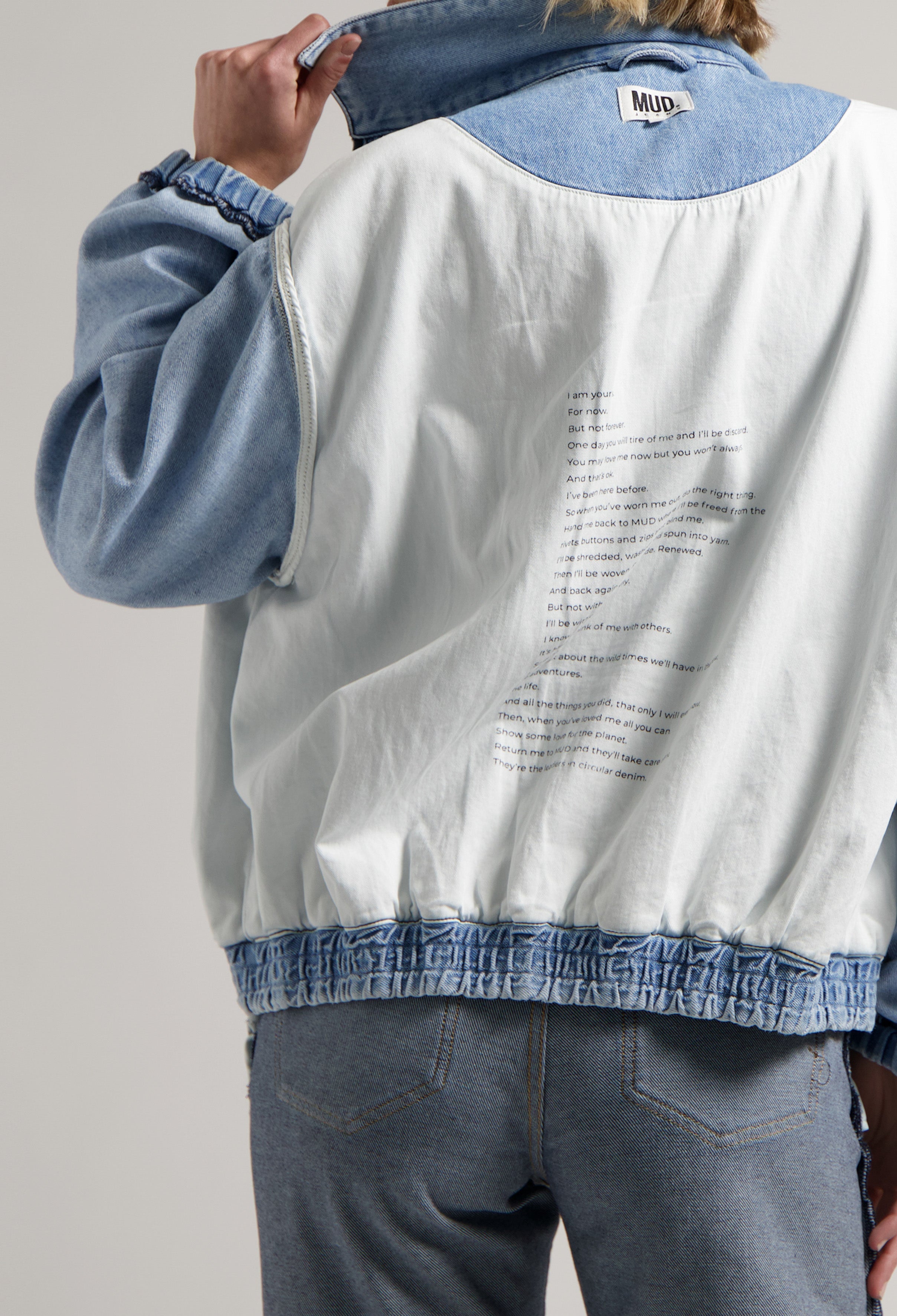 White and blue reversible denim jacket with text detail, worn over light blue jeans, highlighting sustainable MUD fashion.