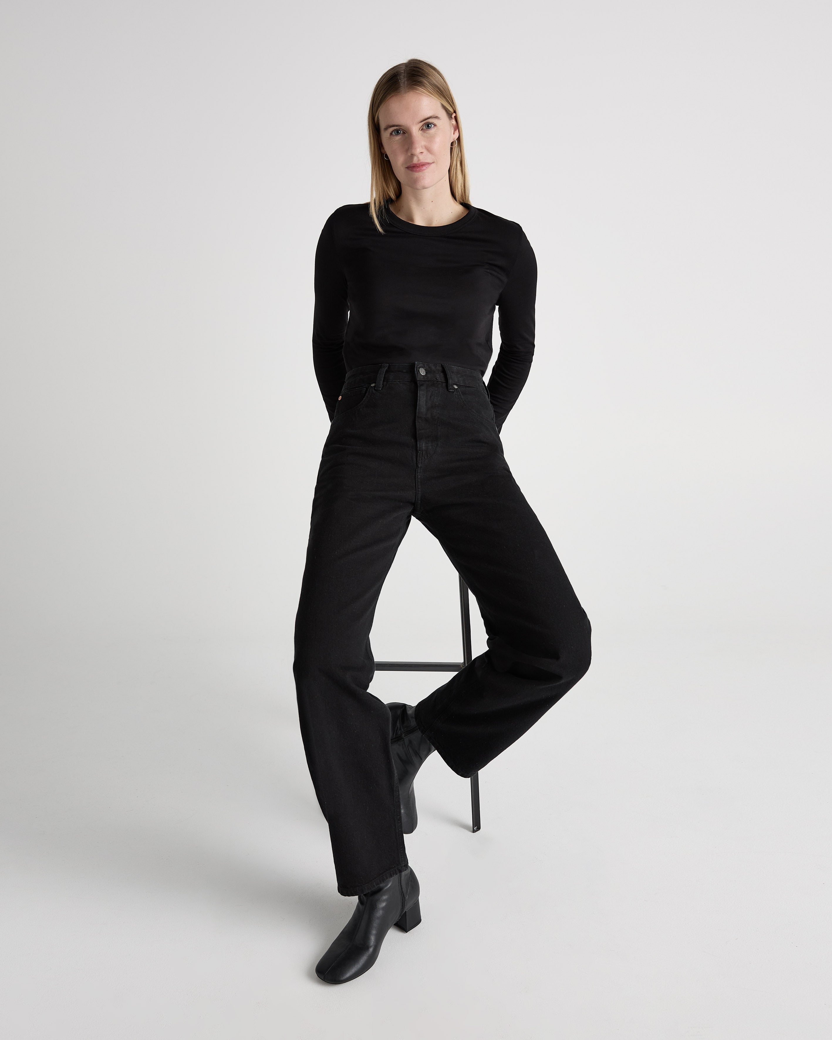 A model wearing high-waisted black jeans and a long-sleeve black top, paired with stylish black ankle boots.