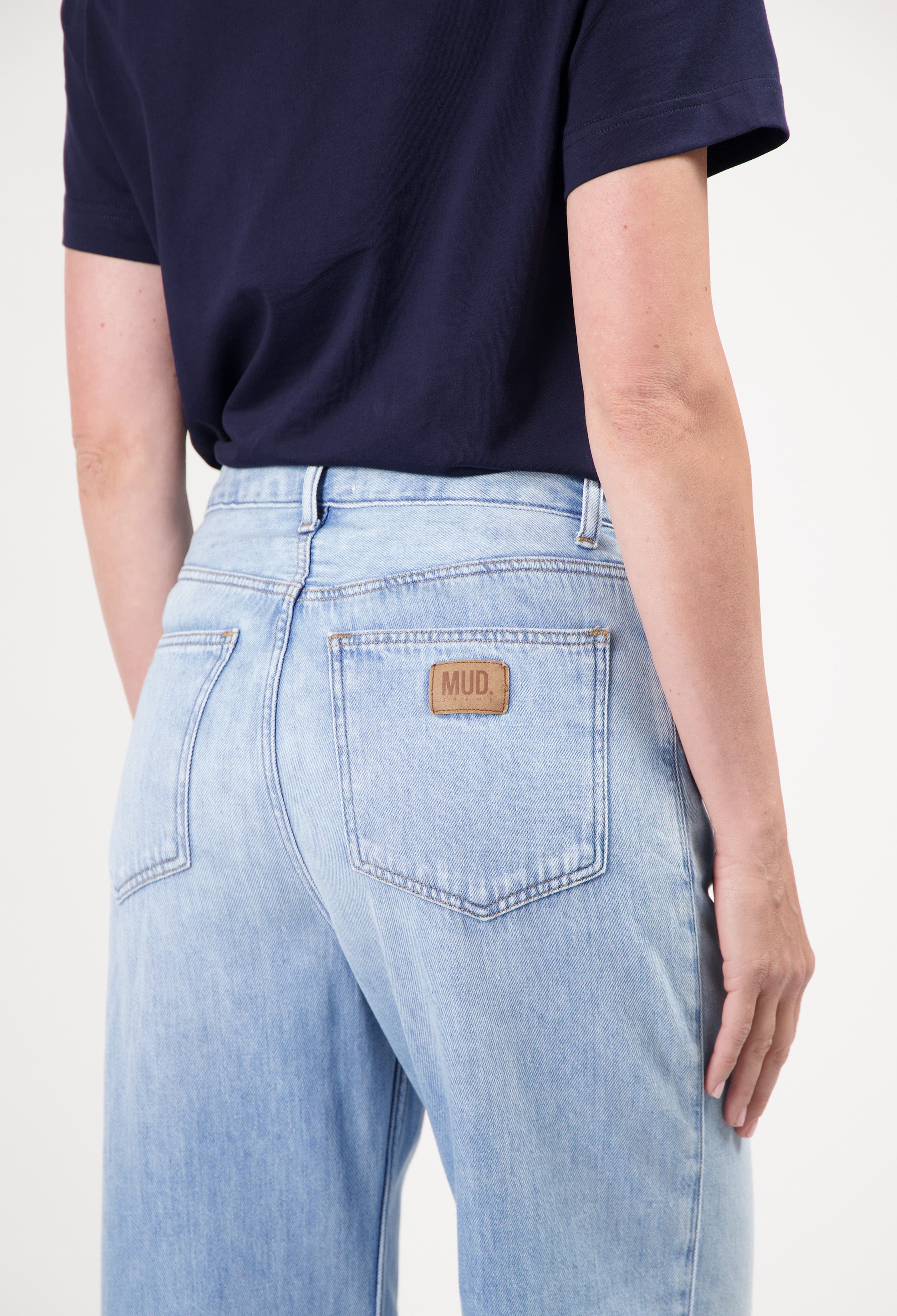 Light blue sustainable MUD Jeans showcasing the back pocket and logo detail, worn with a dark navy short-sleeve top.