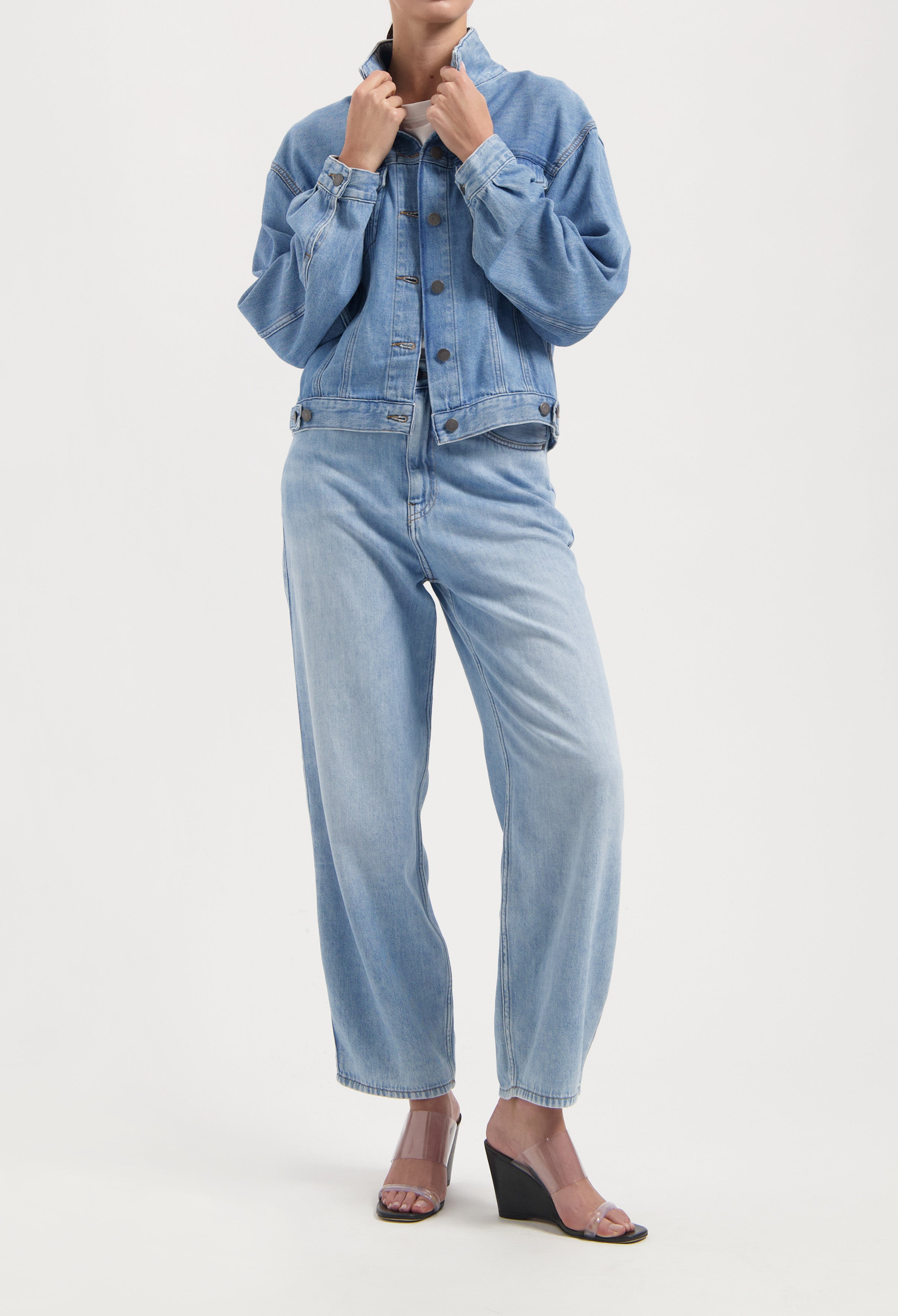 Light blue denim jacket and jeans ensemble, highlighting a relaxed fit, paired with clear wedge sandals on a minimal background.
