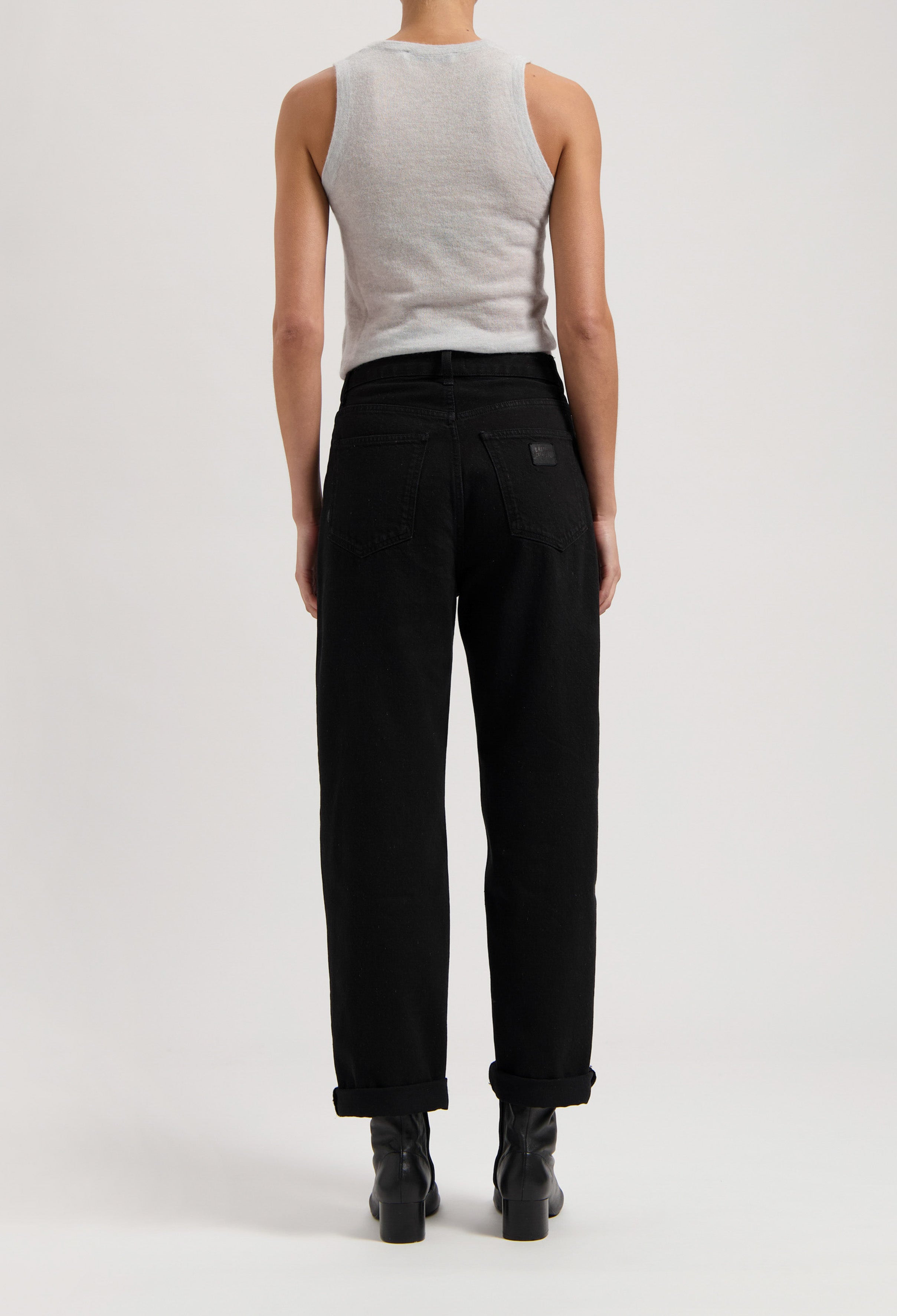 Back view of model wearing black high-waisted jeans paired with a gray sleeveless top, showcasing modern casual fashion style.