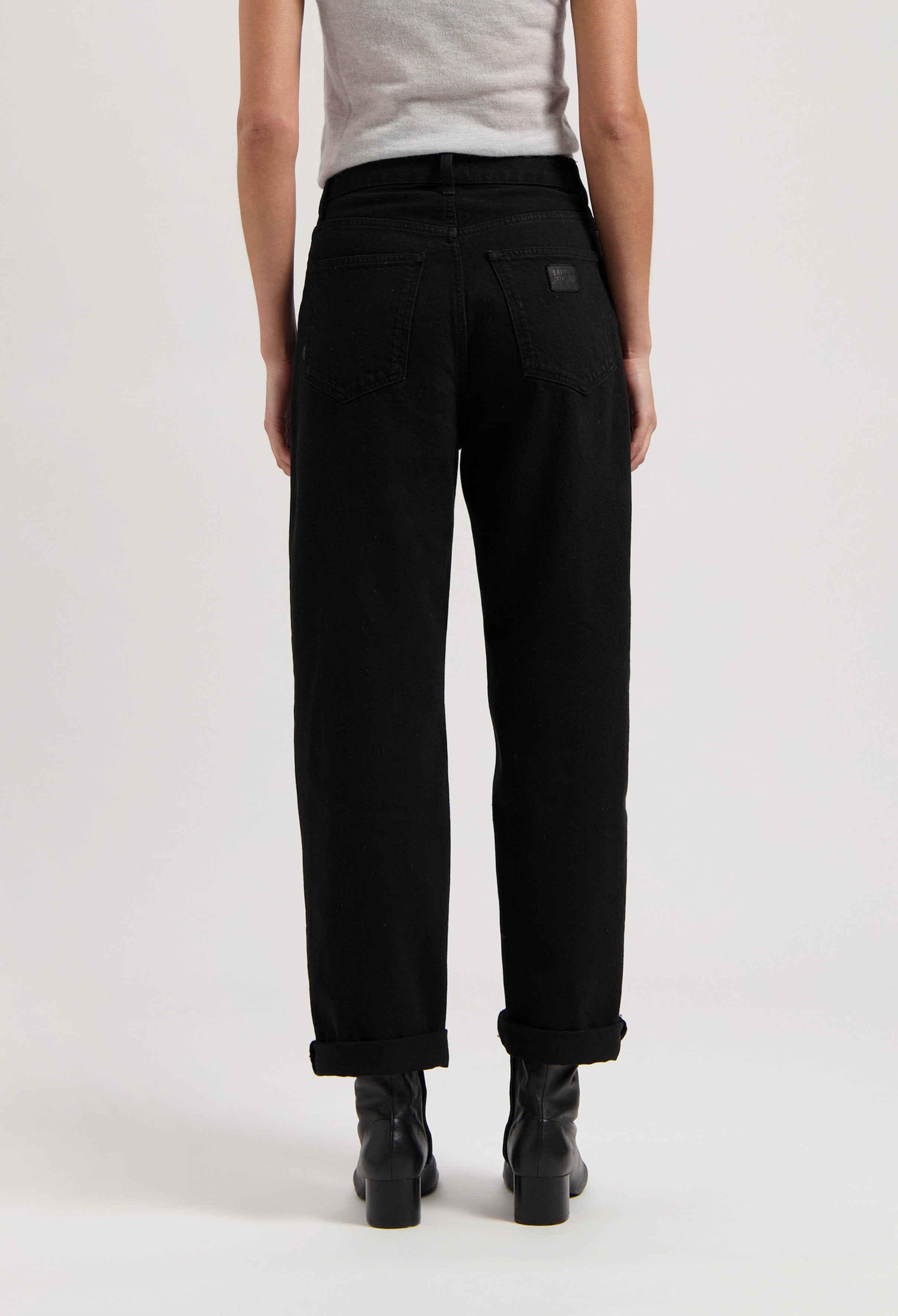 Black high-waisted jeans made of cotton, shown from the back, paired with black boots and a light gray sleeveless top.