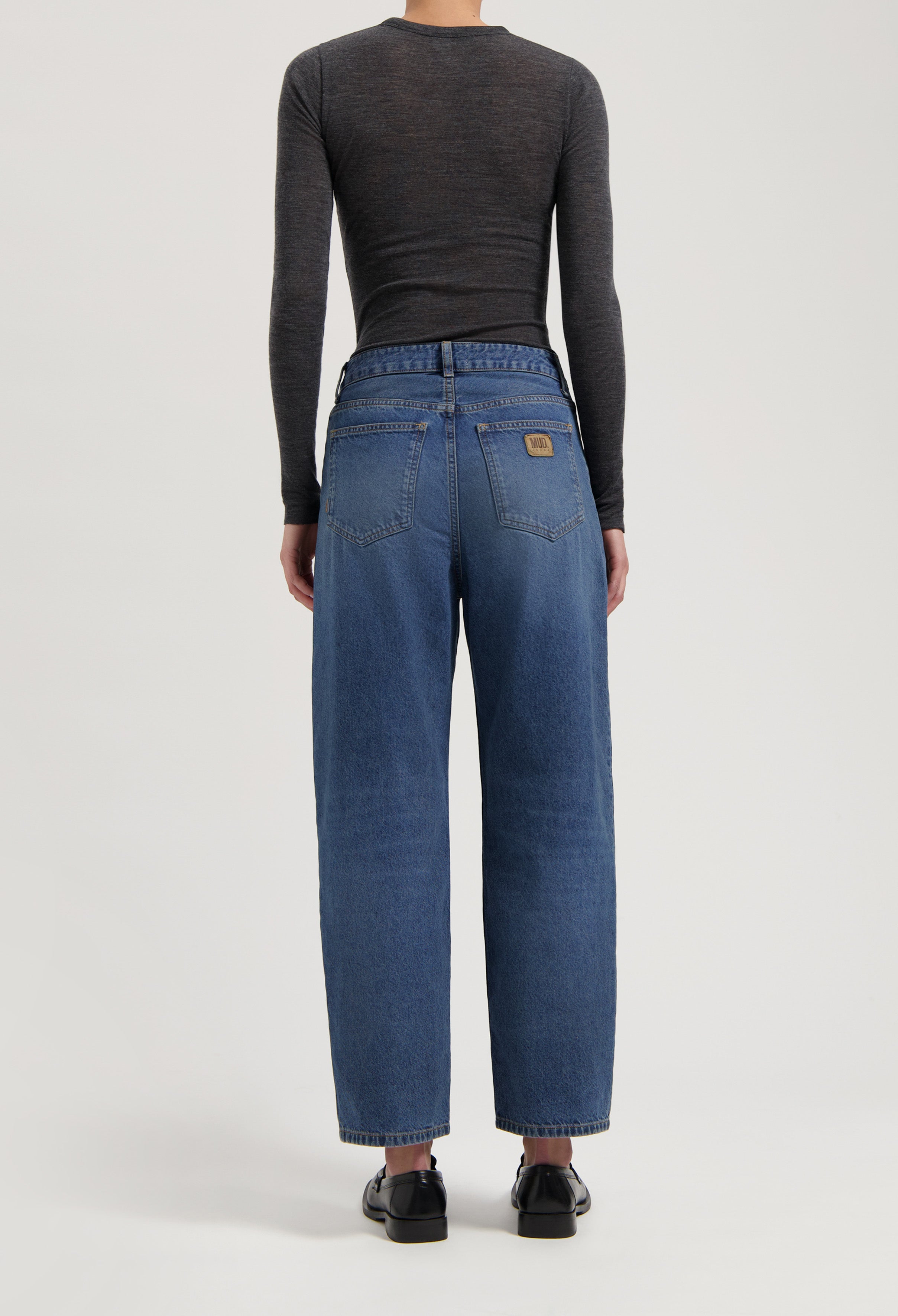 High-rise blue denim jeans made from organic cotton, worn with a fitted dark gray long-sleeve top and black loafers.