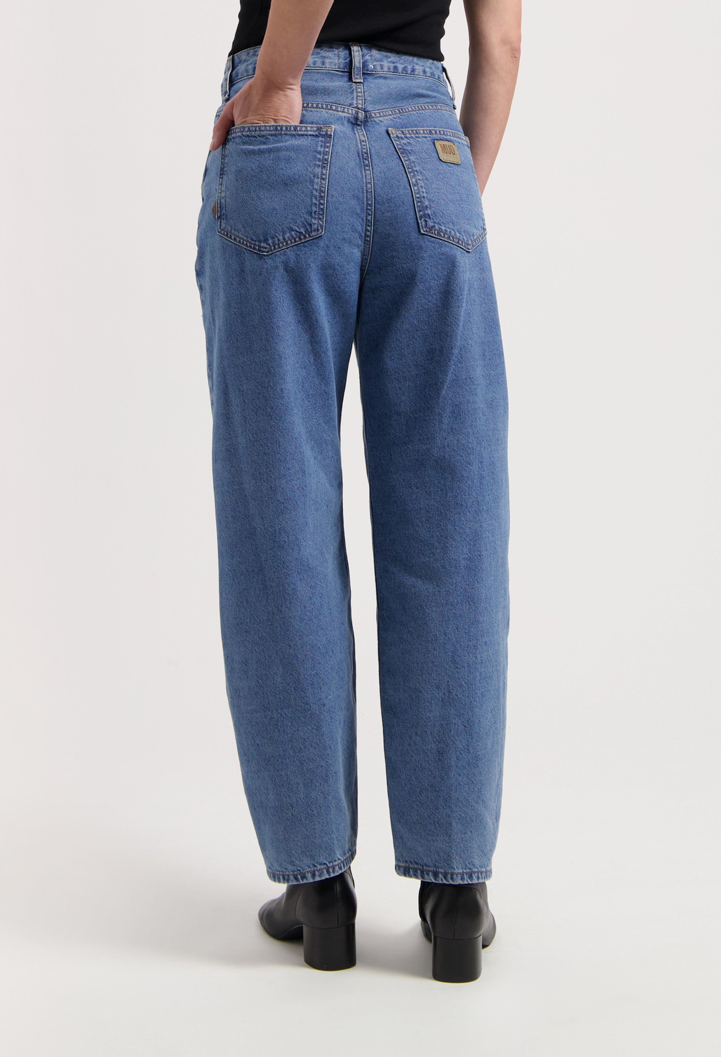 Loose-fit blue denim jeans from MUD Jeans, featuring a high-waisted cut, paired with black heeled boots.