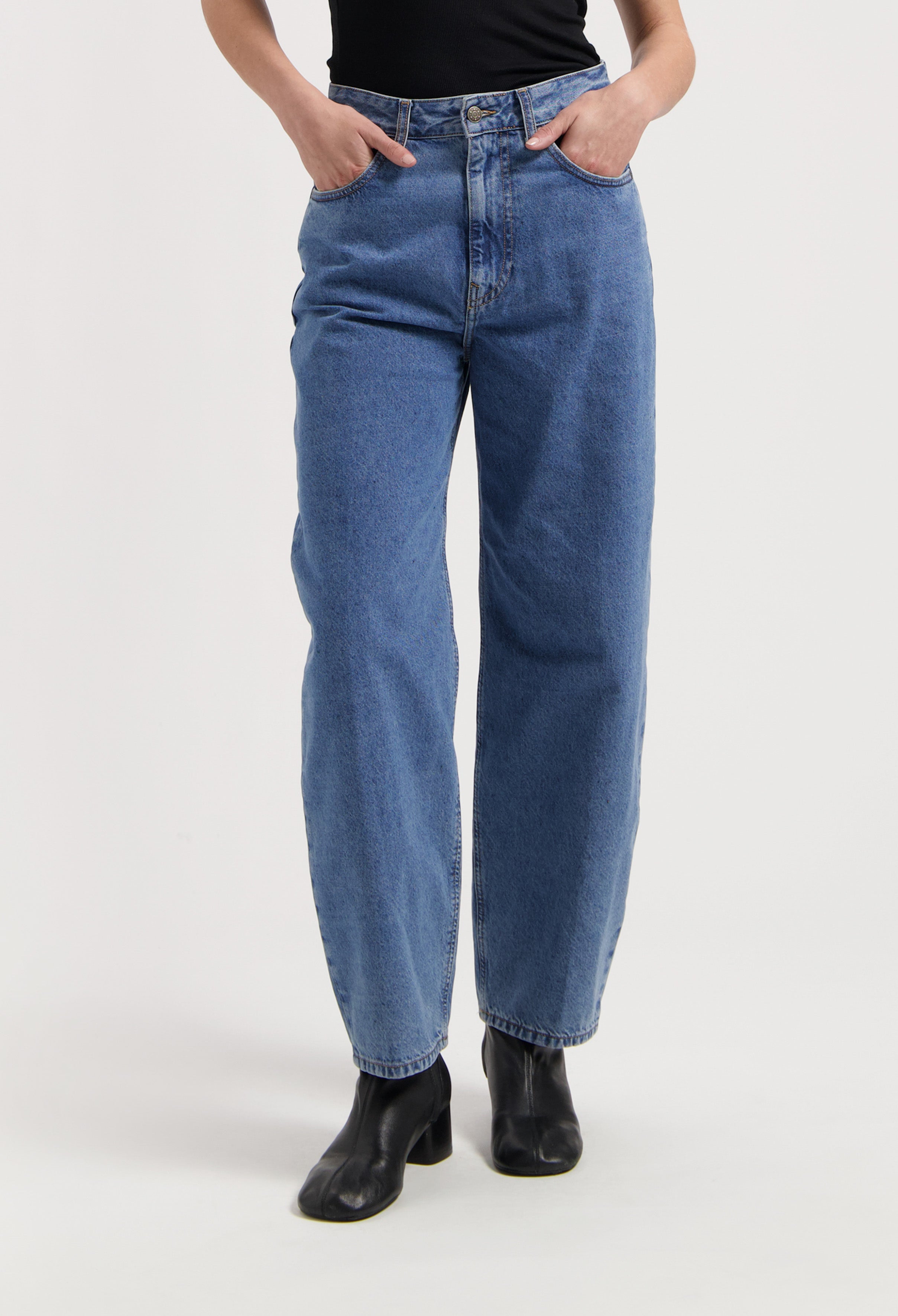 High-waisted, loose-fit, blue denim jeans paired with a black sleeveless top and black ankle boots.