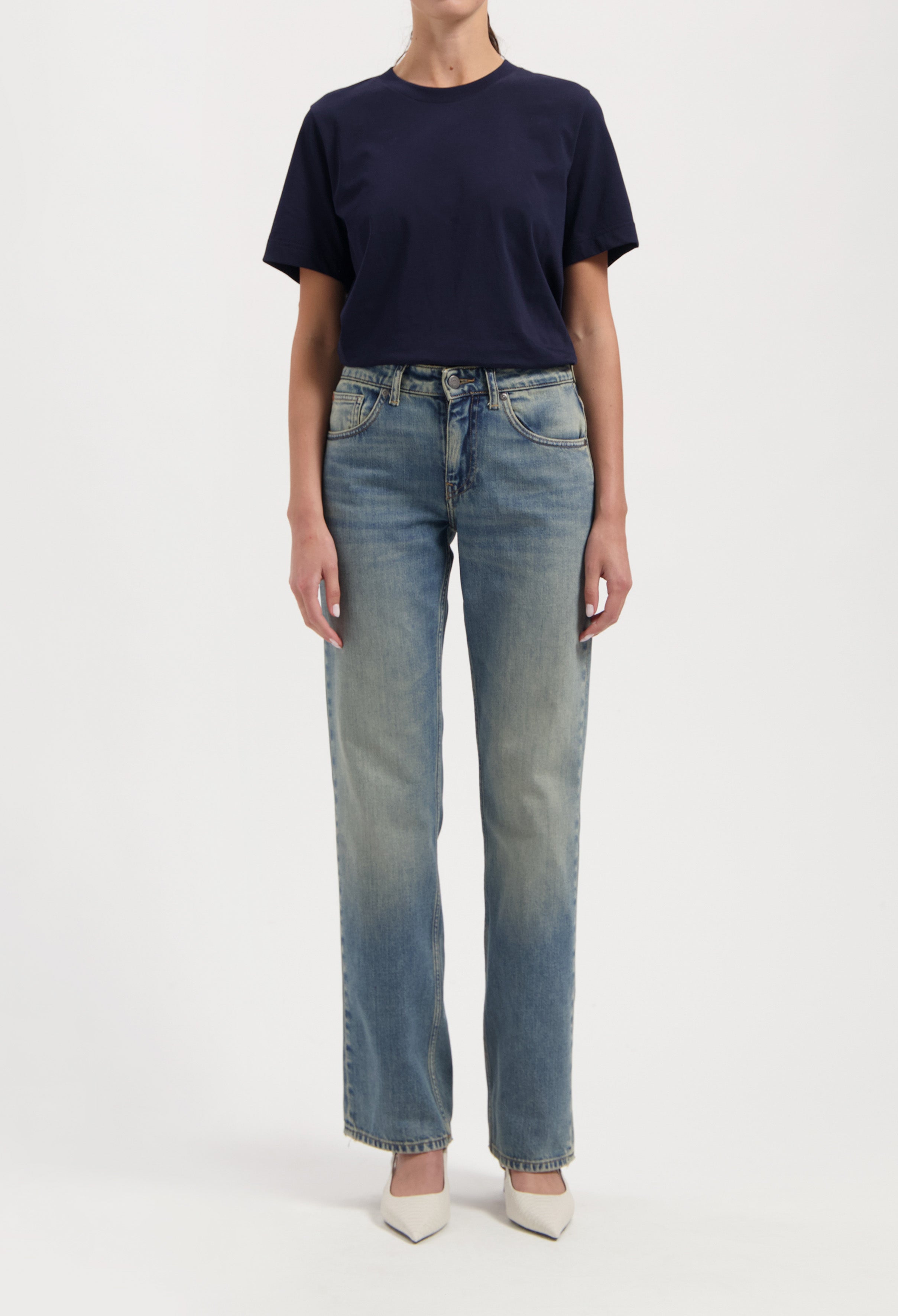 Casual outfit with a navy blue T-shirt paired with light-washed straight-leg jeans and white pointed-toe heels.