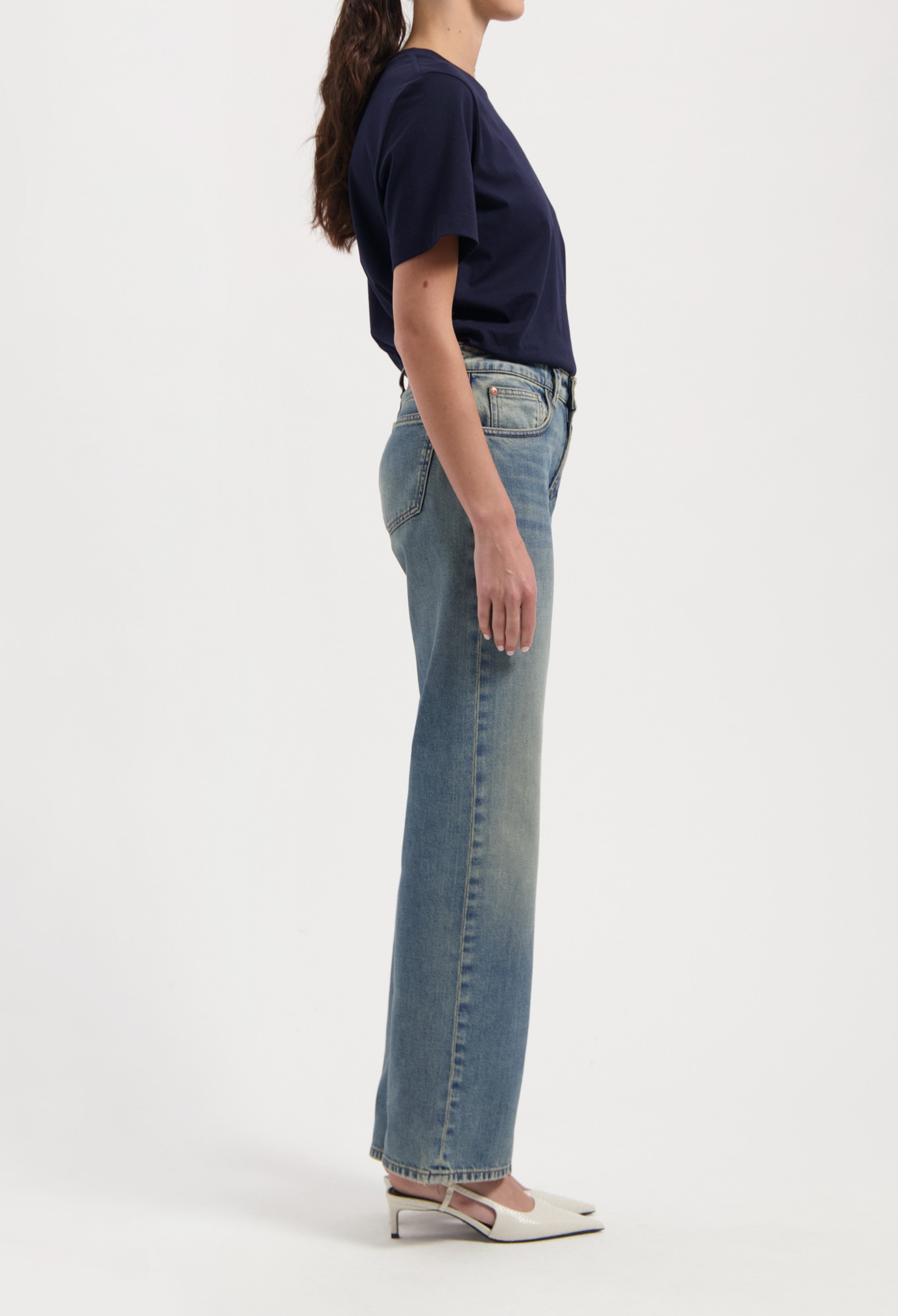 Women's classic blue denim jeans paired with a navy short-sleeve top and white pointed heels, side view.