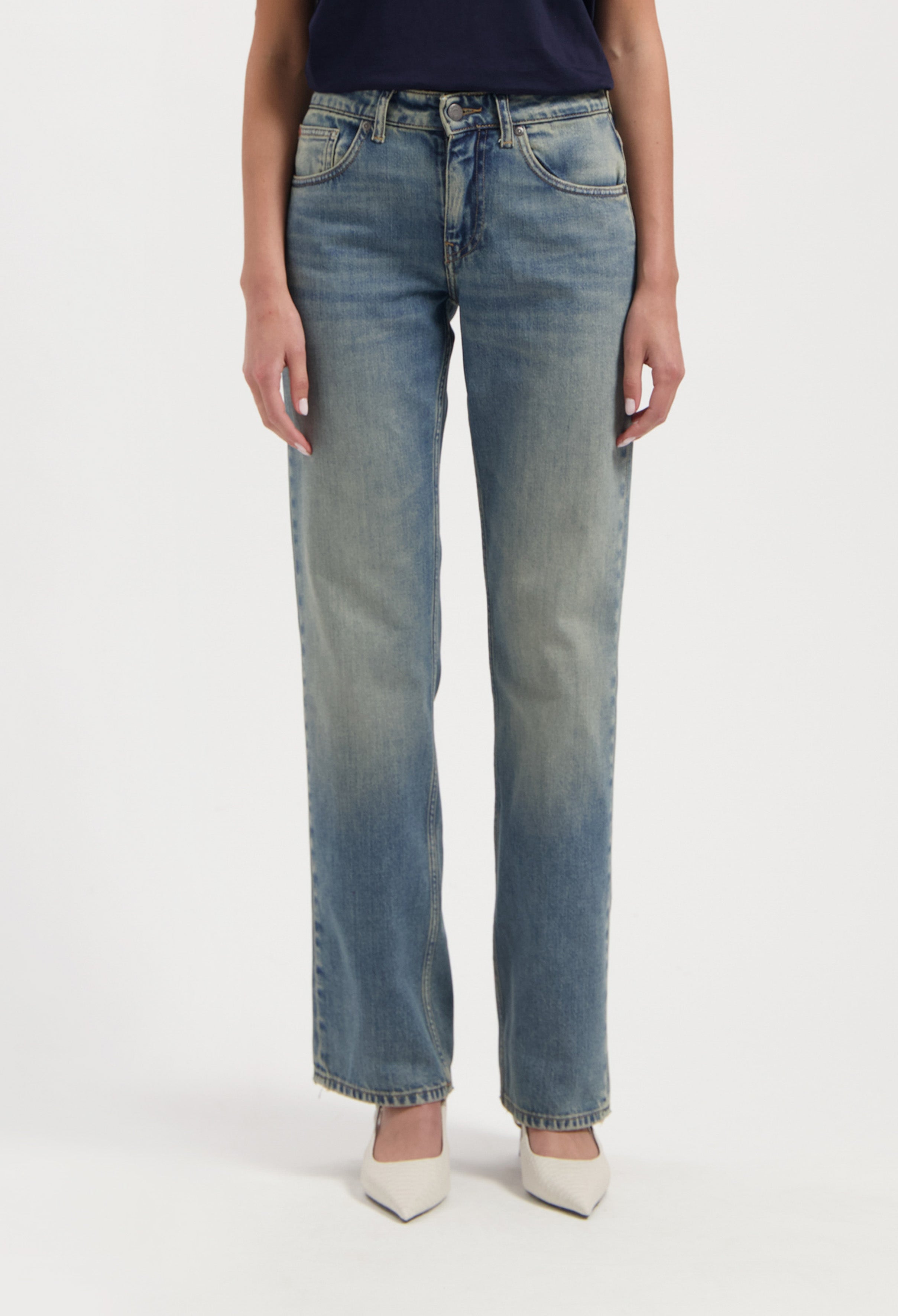 Light blue, straight-leg denim jeans made from cotton, worn with a dark navy top and white pointed-toe heels.