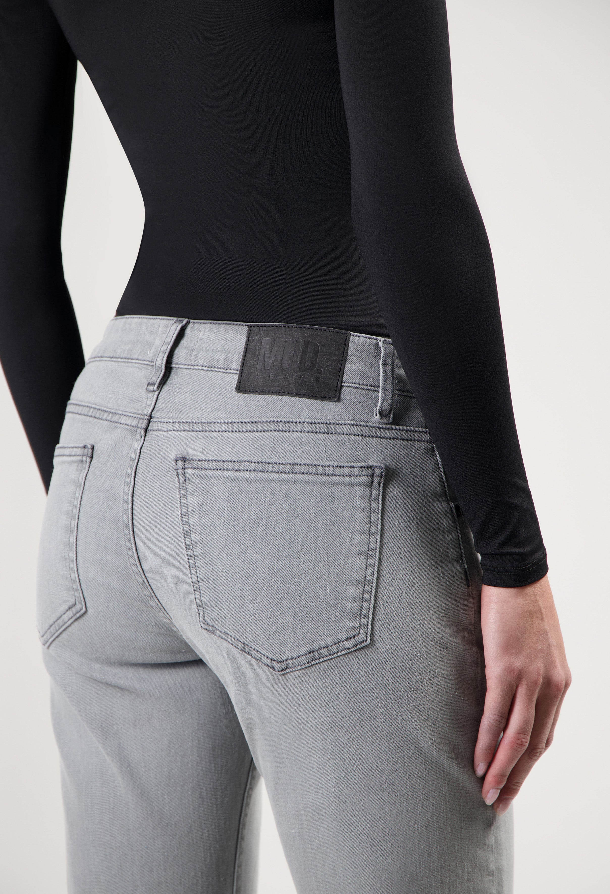 Gray MUD Jeans made from sustainable materials, featuring a rear view of high-waisted denim with a black long-sleeve top.
