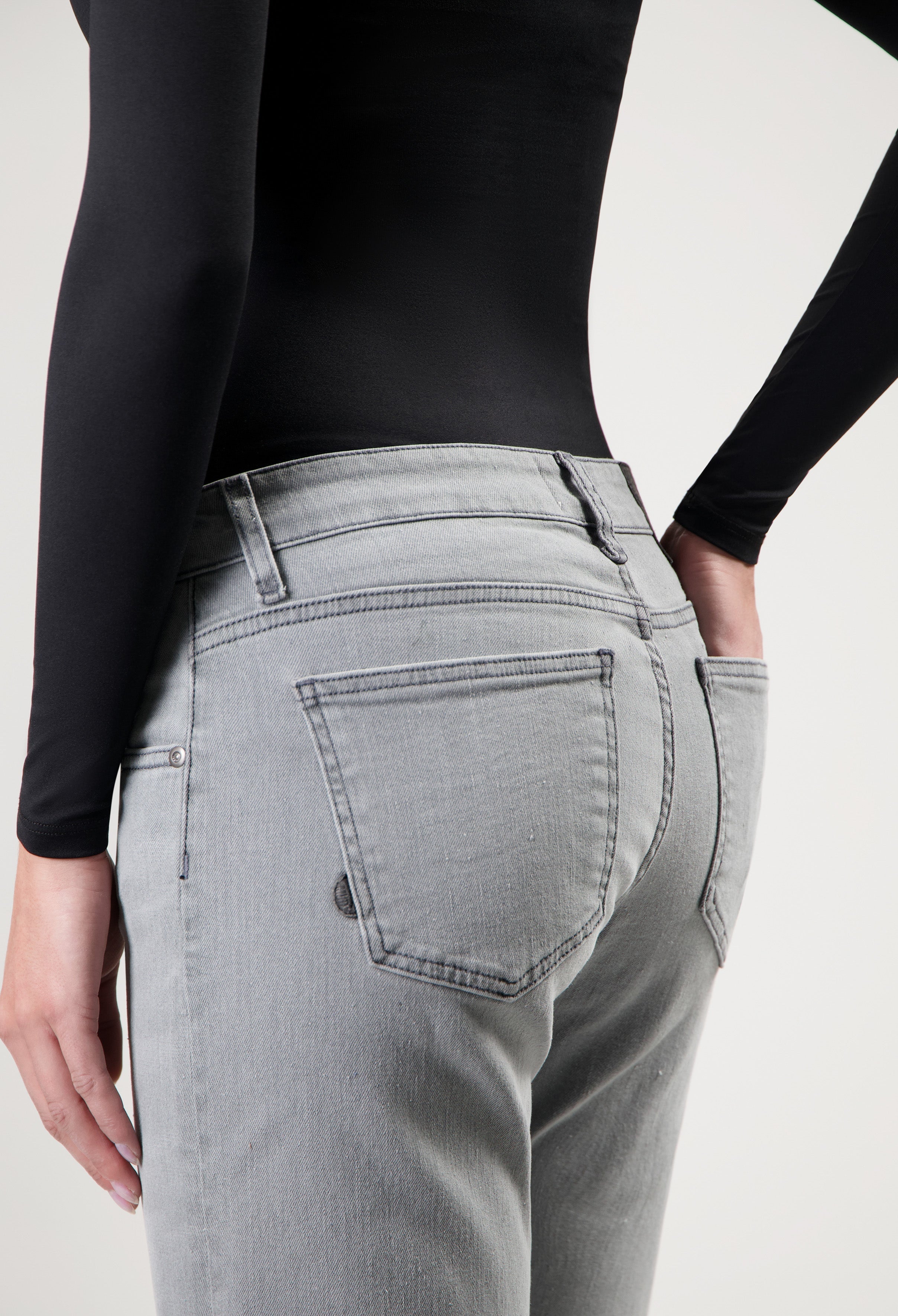 Person wearing light gray jeans with back pockets, styled with a black long-sleeve top, showcasing casual fashion.