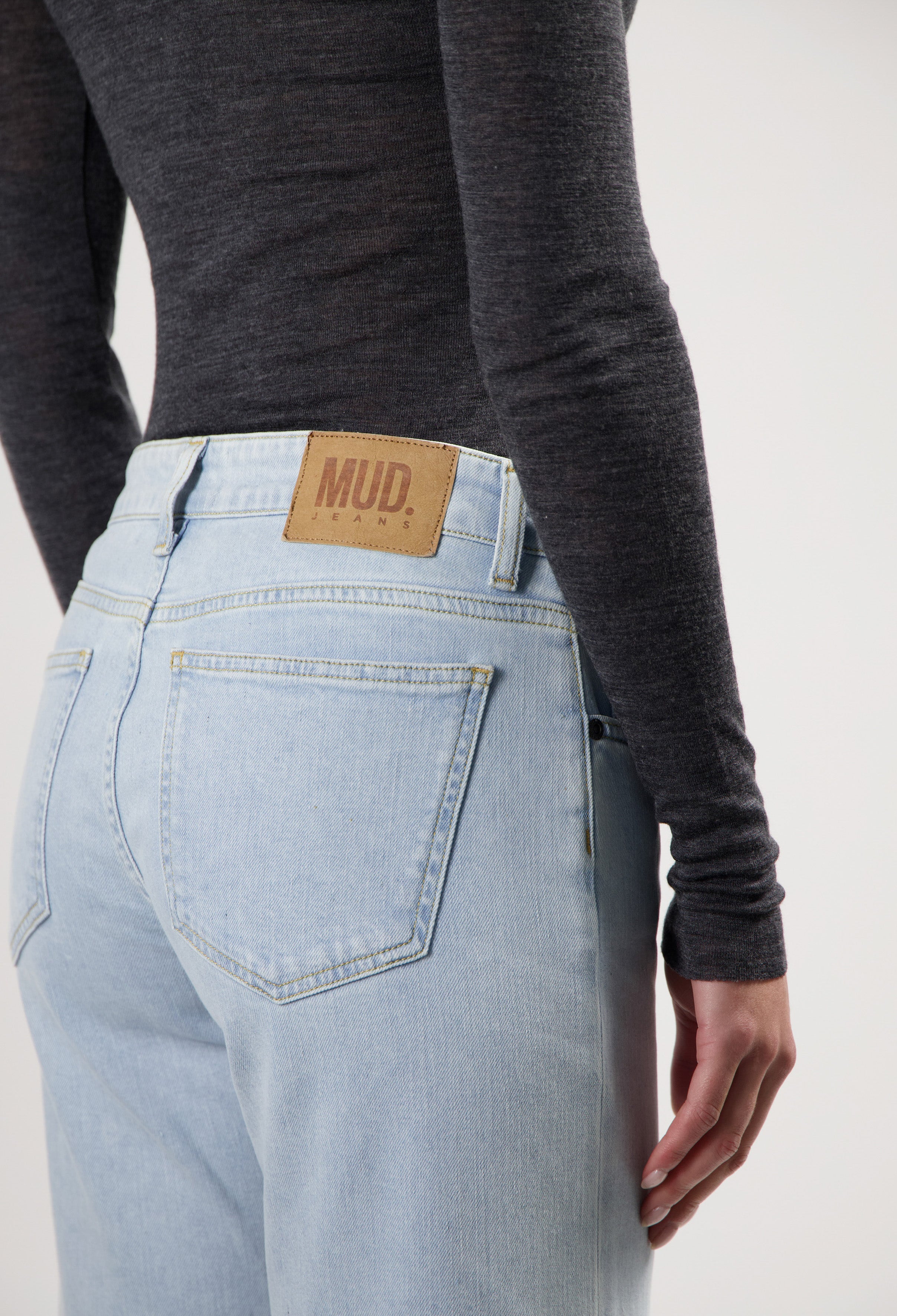 Light blue MUD Jeans made from organic cotton, showcasing a casual fit with a brown leather patch, paired with a dark gray top.