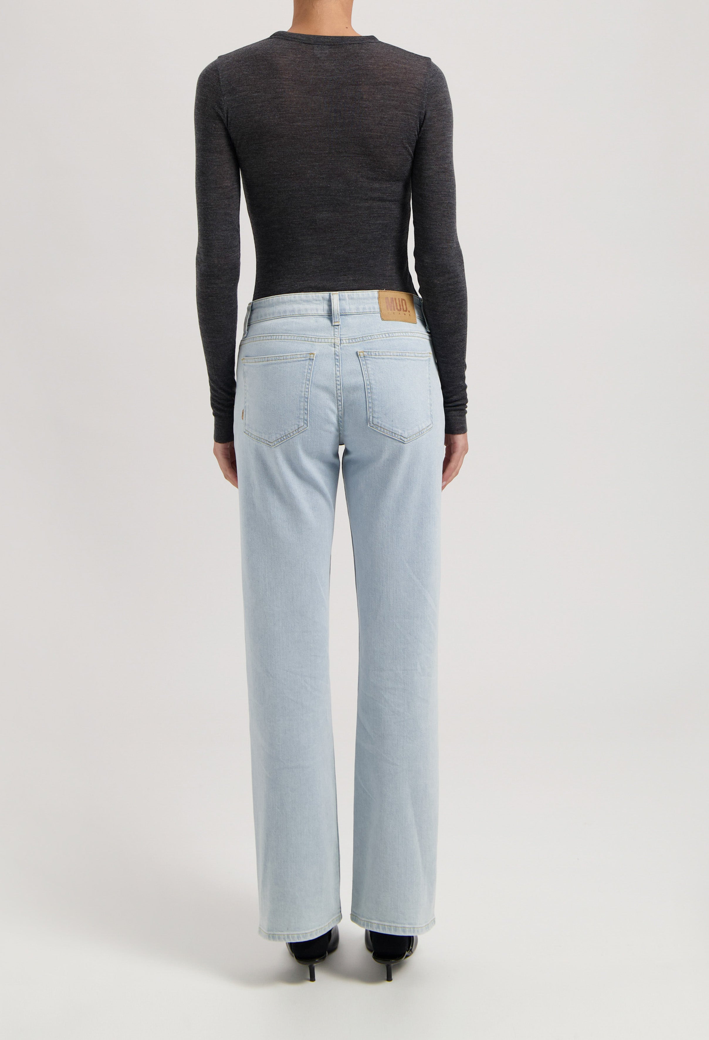 Back view of MUD Jeans in light blue, relaxed-fit denim worn with a fitted long-sleeve black top, emphasizing sustainable fashion.