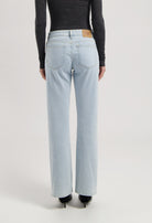 Back view of light blue, straight-leg jeans from MUD Jeans, paired with a dark gray long-sleeve top and black heels.