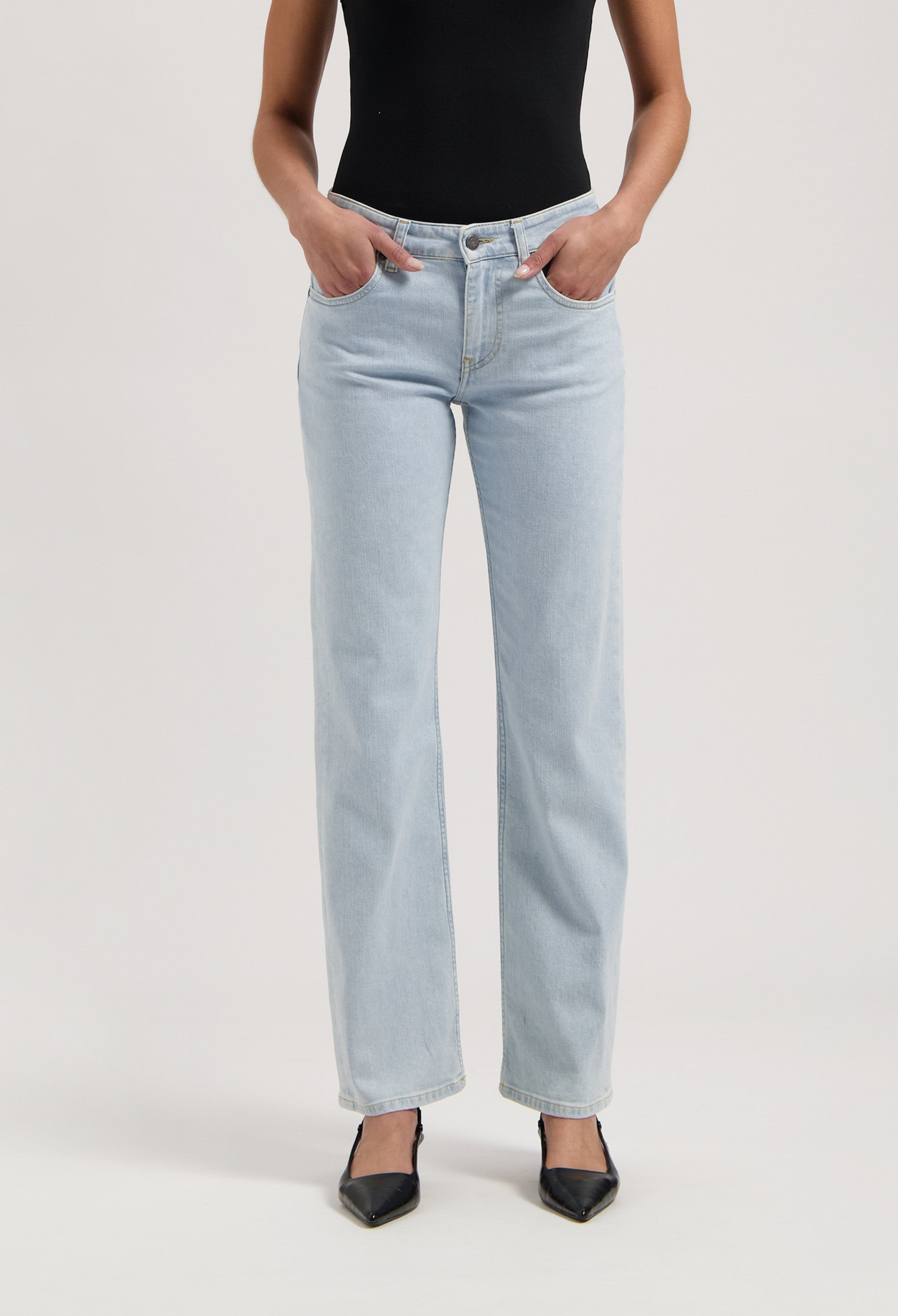 Light blue, high-waisted jeans in a classic fit, paired with a black sleeveless top and pointed black heels.