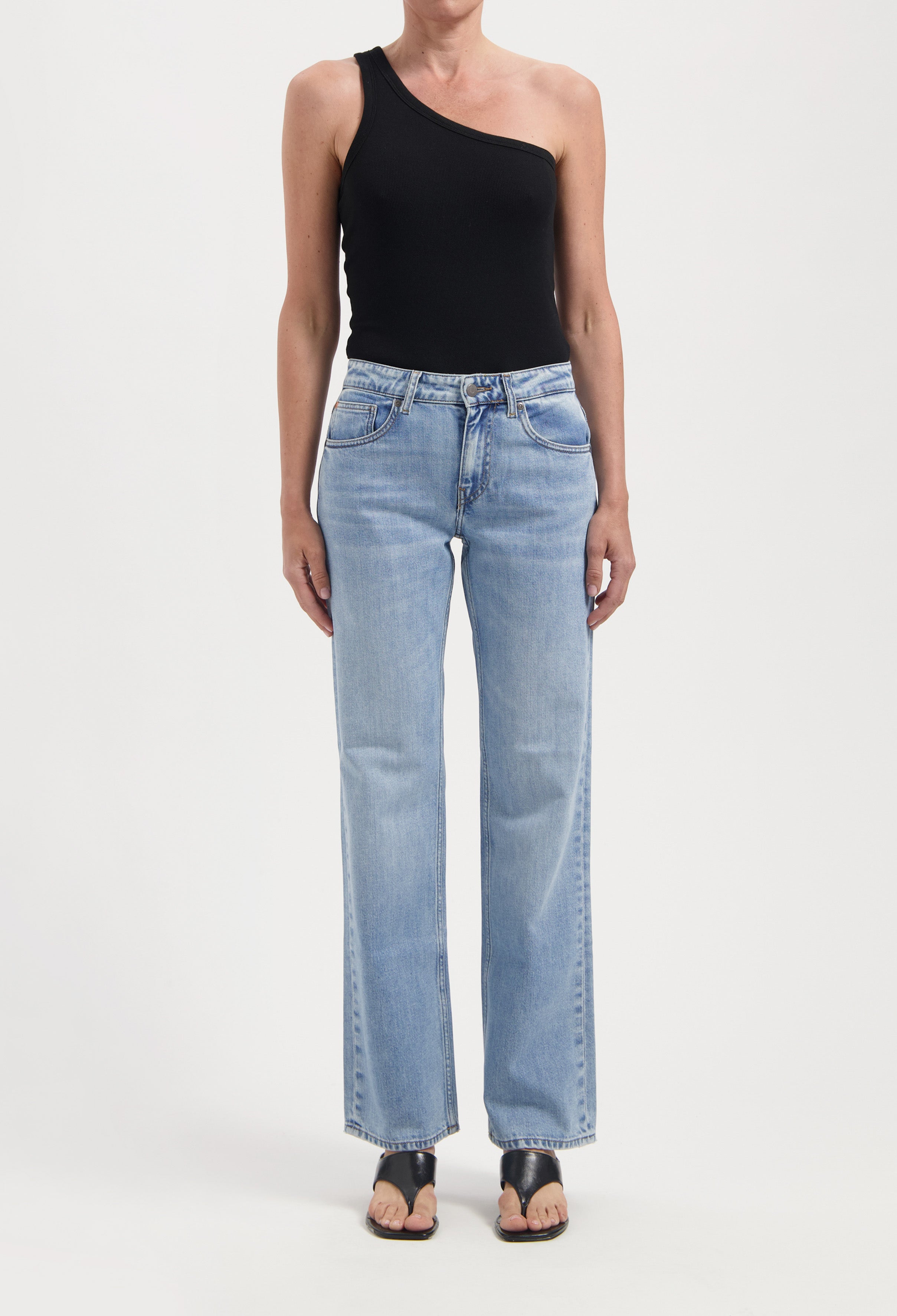A black one-shoulder top paired with light blue, straight-leg jeans and black sandals on a white background.