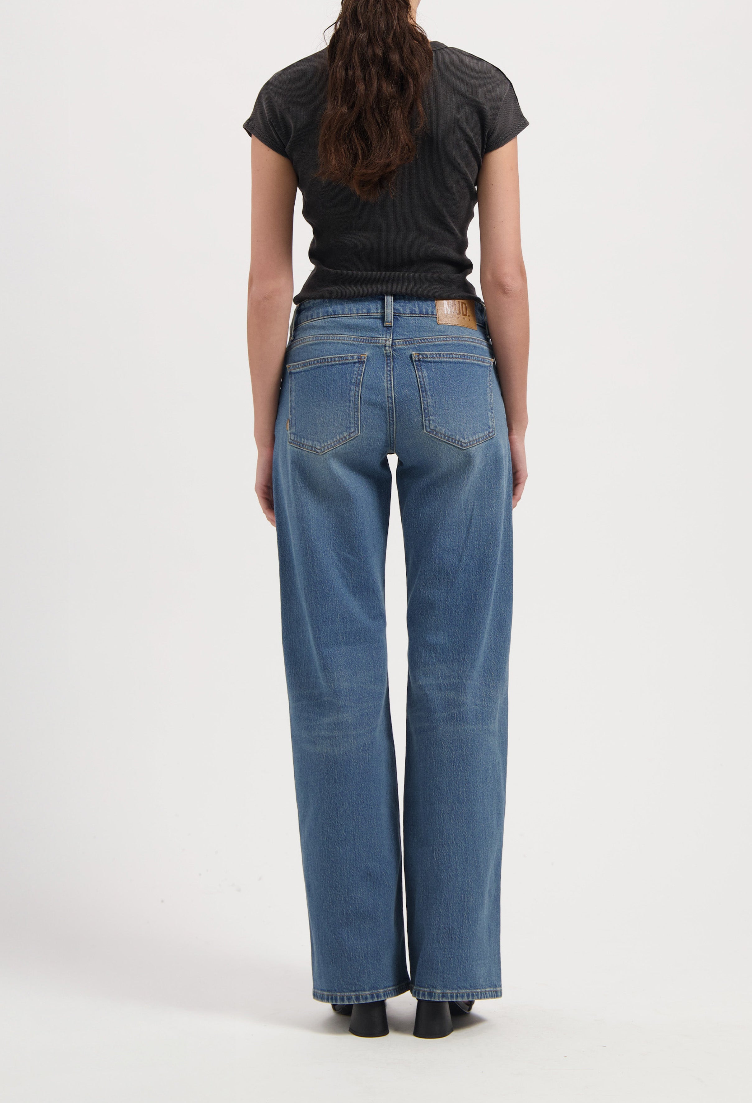 Back view of a model wearing eco-friendly MUD Jeans, light blue straight-leg denim, paired with a fitted black T-shirt.