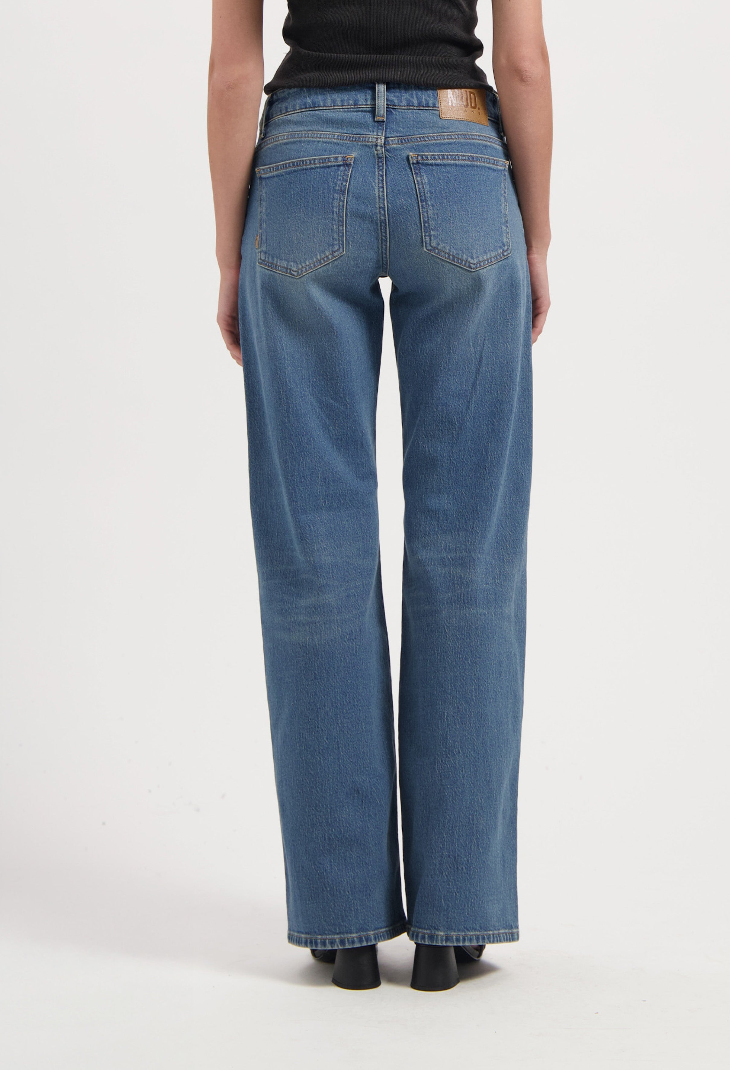 Wide-leg blue jeans made from organic cotton, shown from the back, paired with a black sleeveless top.