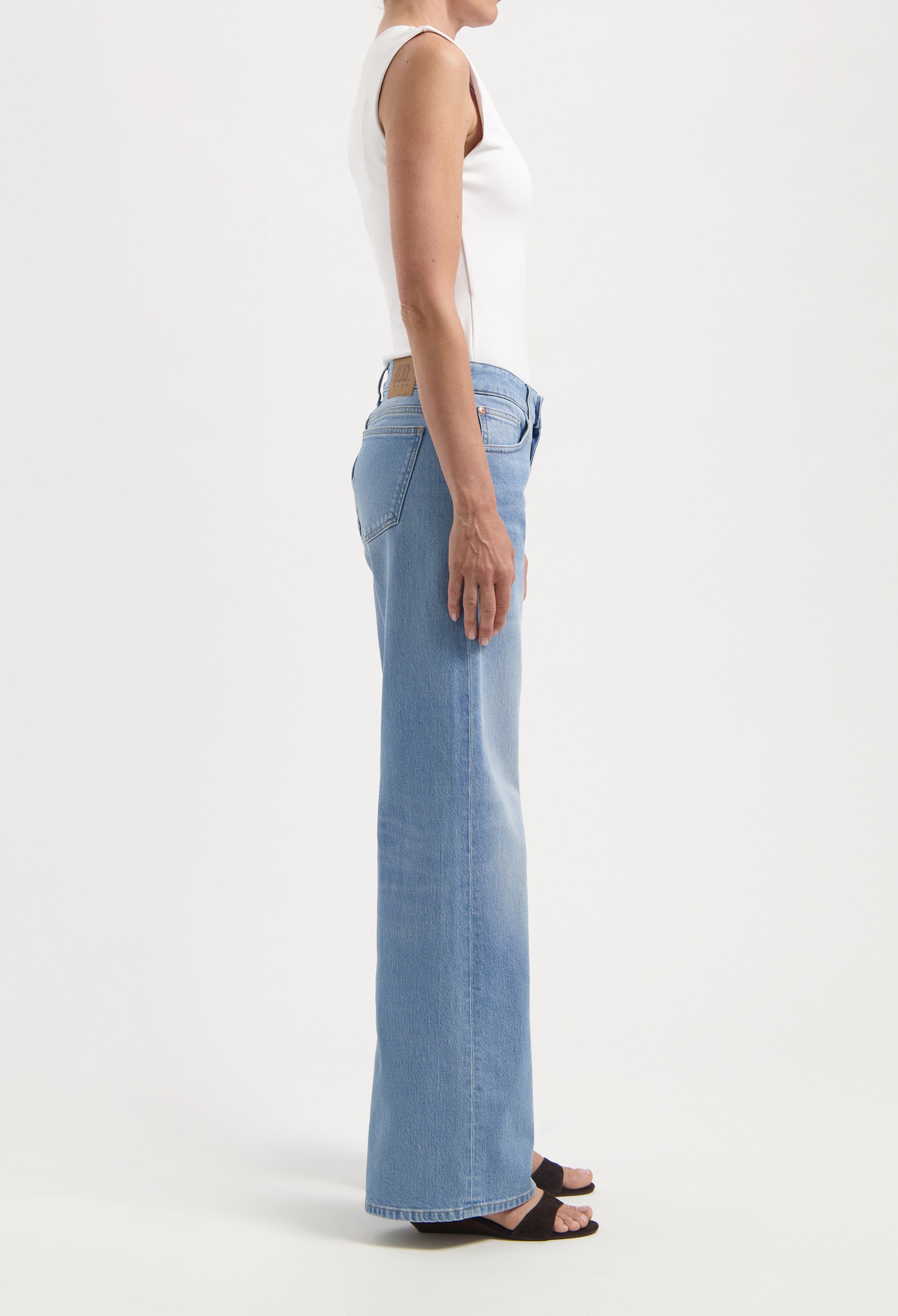 Sleeveless white top paired with light blue, high-waisted straight-leg jeans, side view displaying fit and styling.