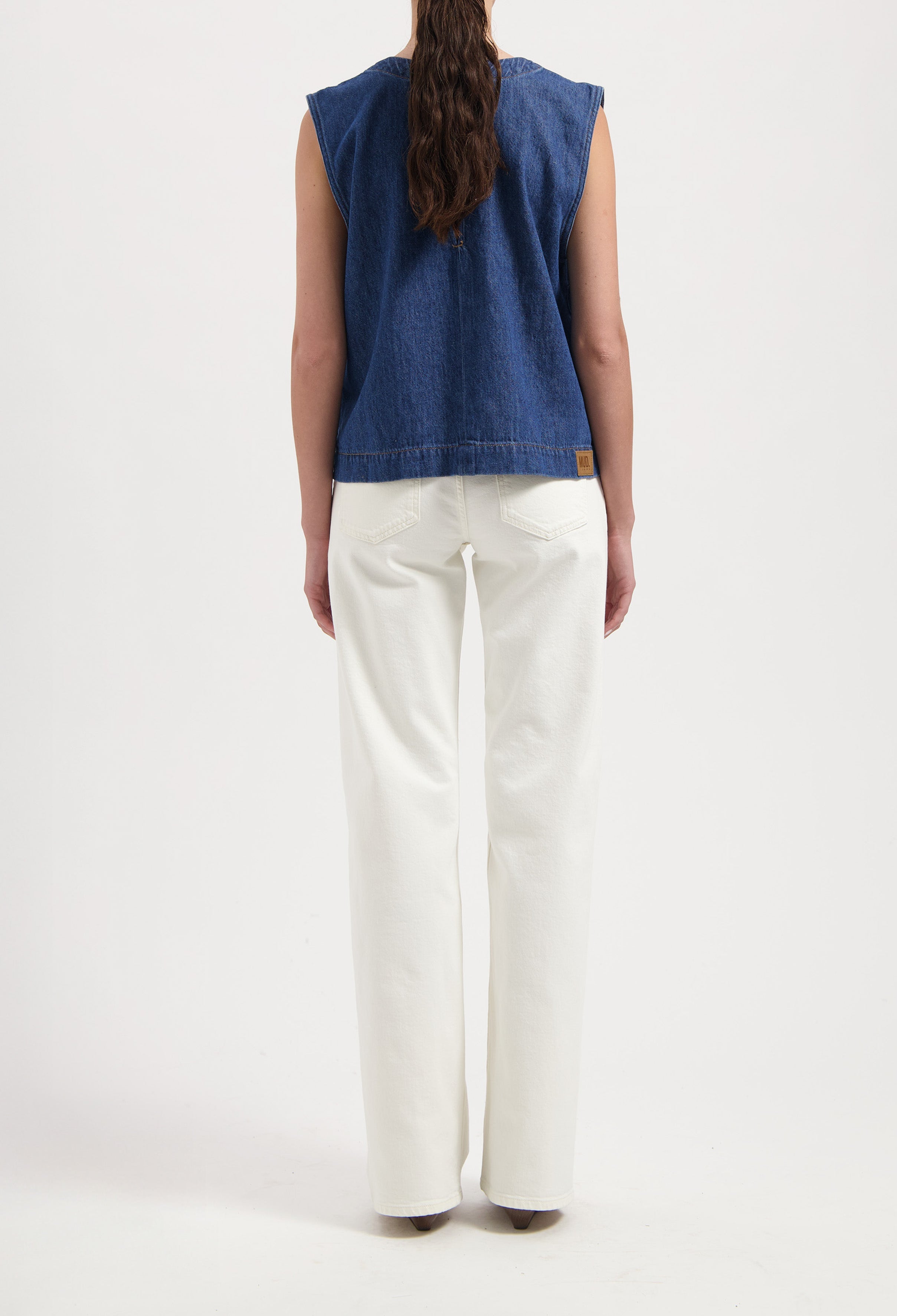 Back view of a denim sleeveless top paired with high-waisted, wide-leg white jeans in a minimalist style.