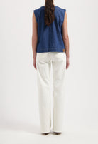 Back view of a denim sleeveless top paired with high-waisted, wide-leg white jeans in a minimalist style.