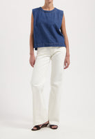 Woman wearing a sleeveless blue denim top and white wide-leg pants, styled with black open-toe sandals.