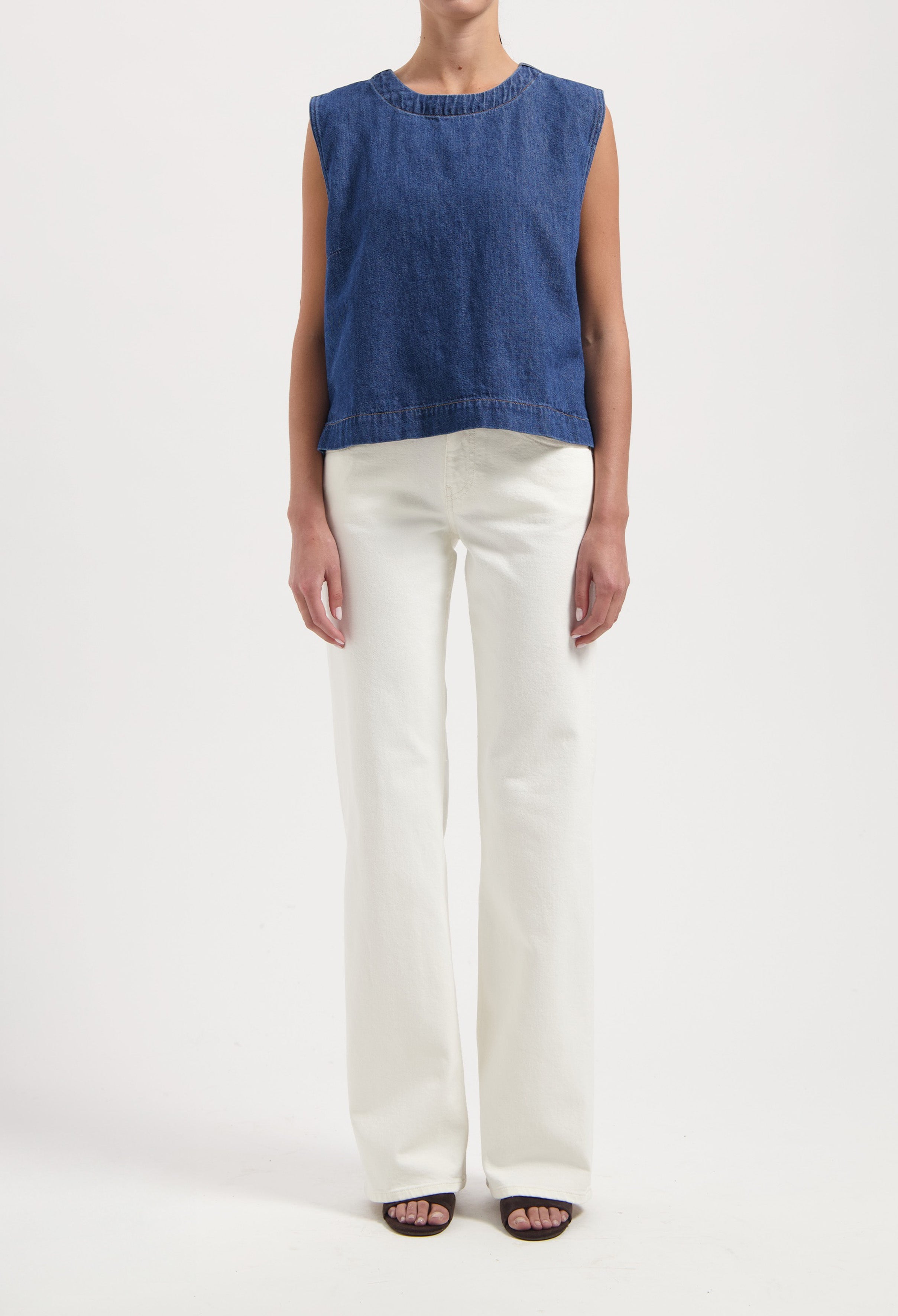 Woman wearing a sleeveless blue denim top paired with high-waisted white wide-leg jeans and black open-toe sandals.