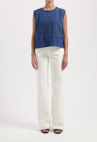 Woman wearing a sleeveless blue denim top paired with high-waisted white wide-leg jeans and black open-toe sandals.