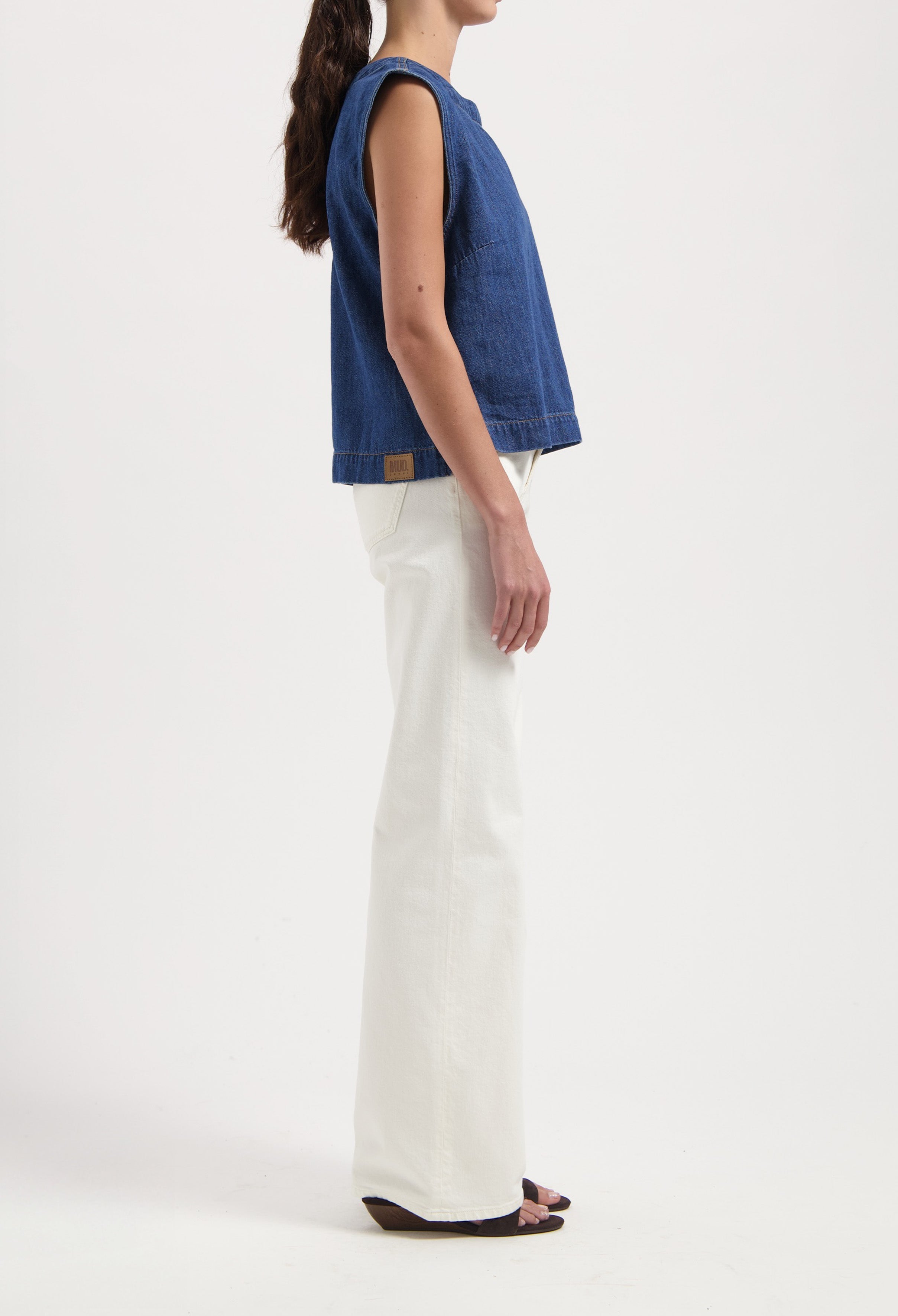 A sleeveless blue denim top paired with white high-waisted, wide-leg jeans, showcasing casual modern fashion.