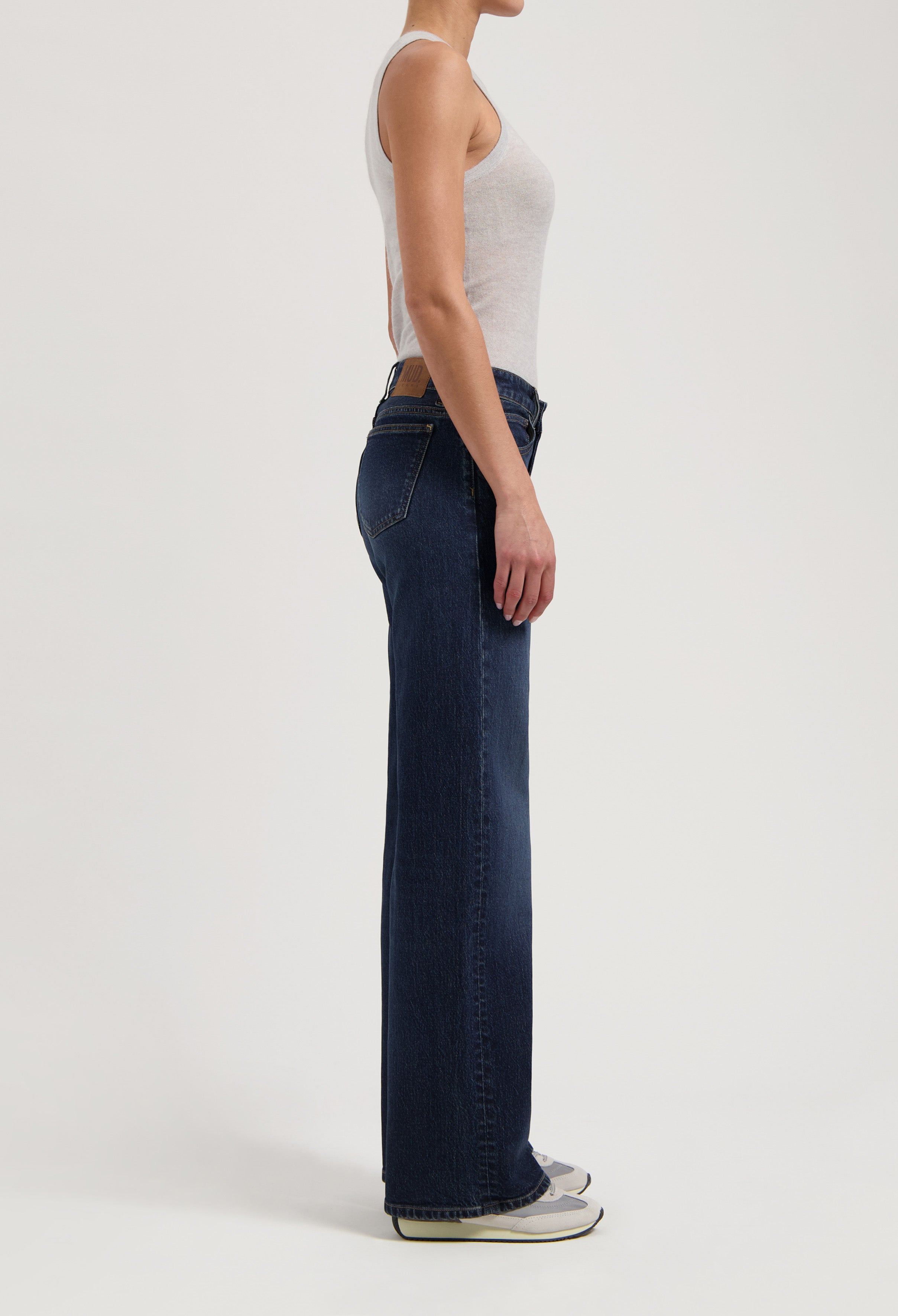 Side view of a woman wearing dark blue straight-leg jeans and a light gray tank top, emphasizing casual fashion style.