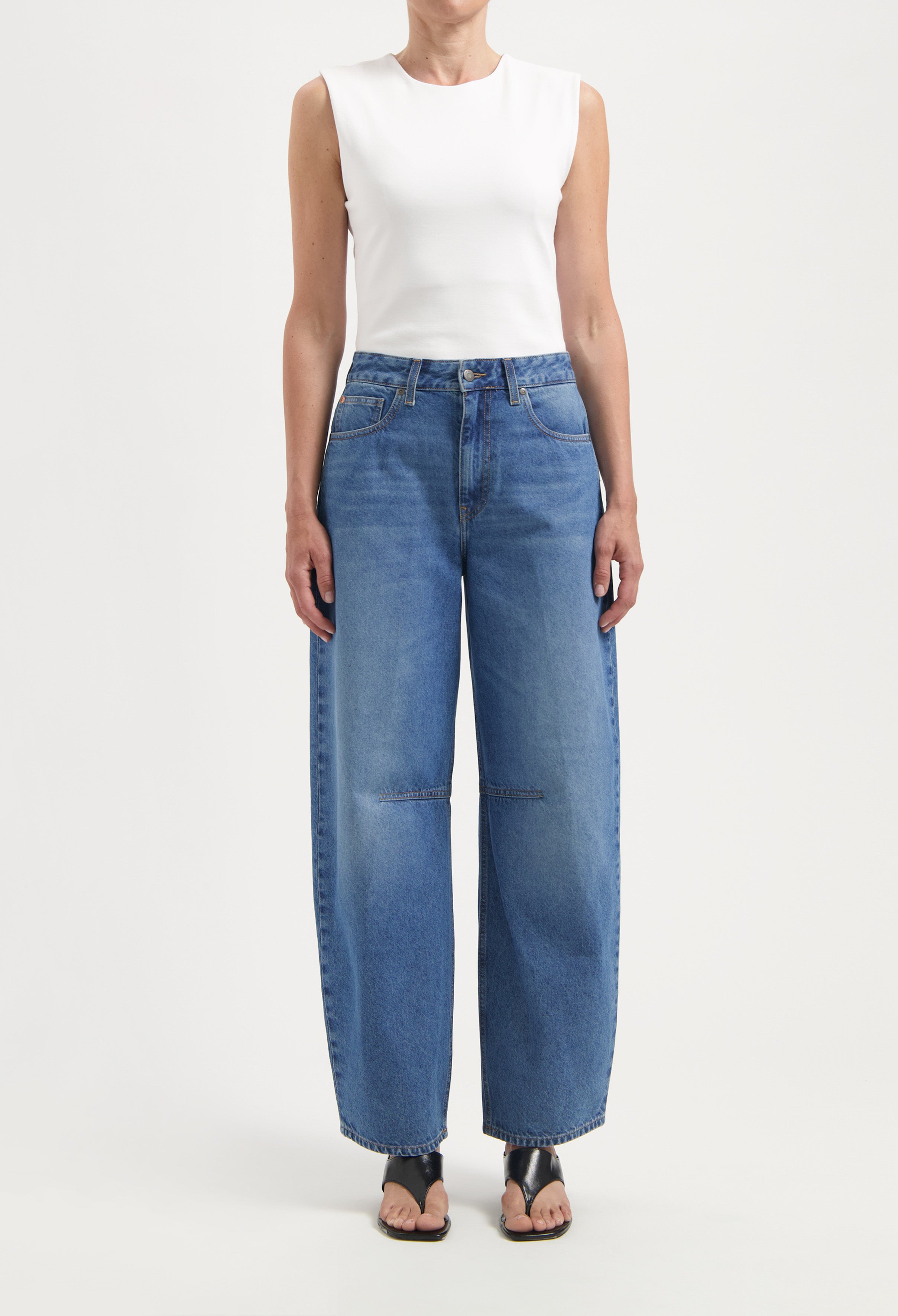 Wide-legged blue denim jeans with pockets and high waist, paired with a sleeveless white top and black sandals.