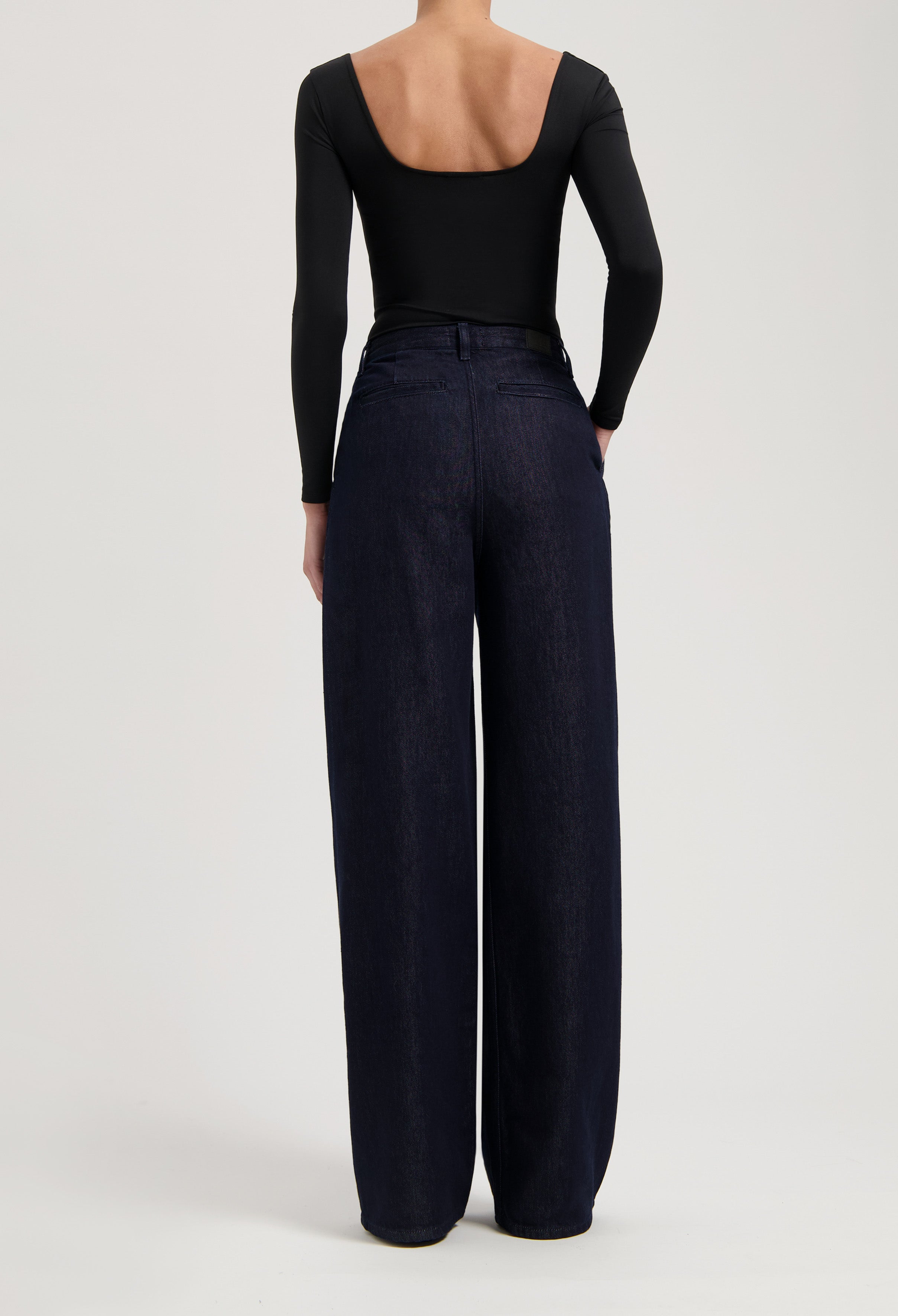 High-waisted wide-leg jeans in dark indigo denim, paired with a sleek black long-sleeve bodysuit featuring an open back.