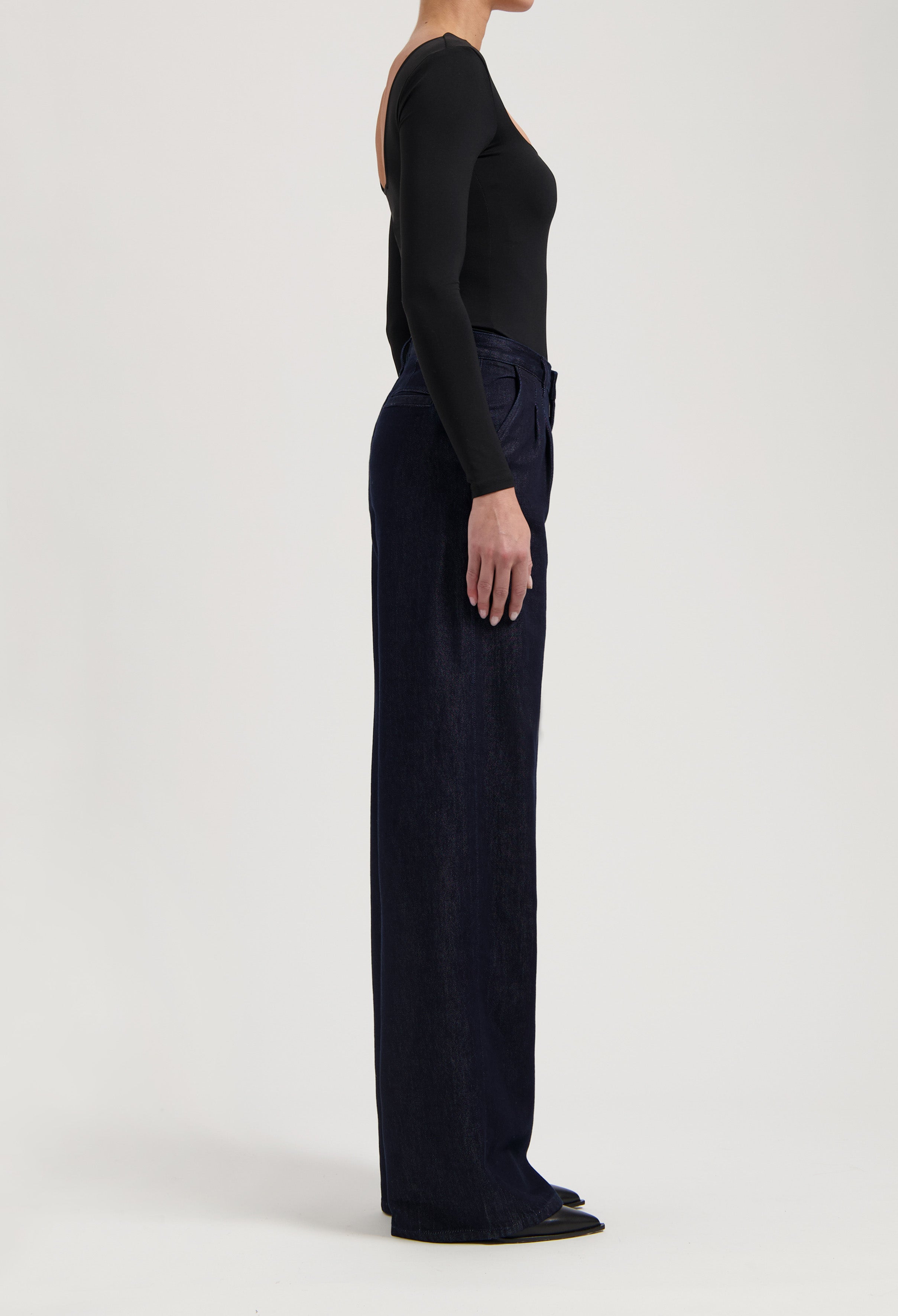 Model in black long-sleeve top and dark blue wide-leg jeans, side profile against plain white background.