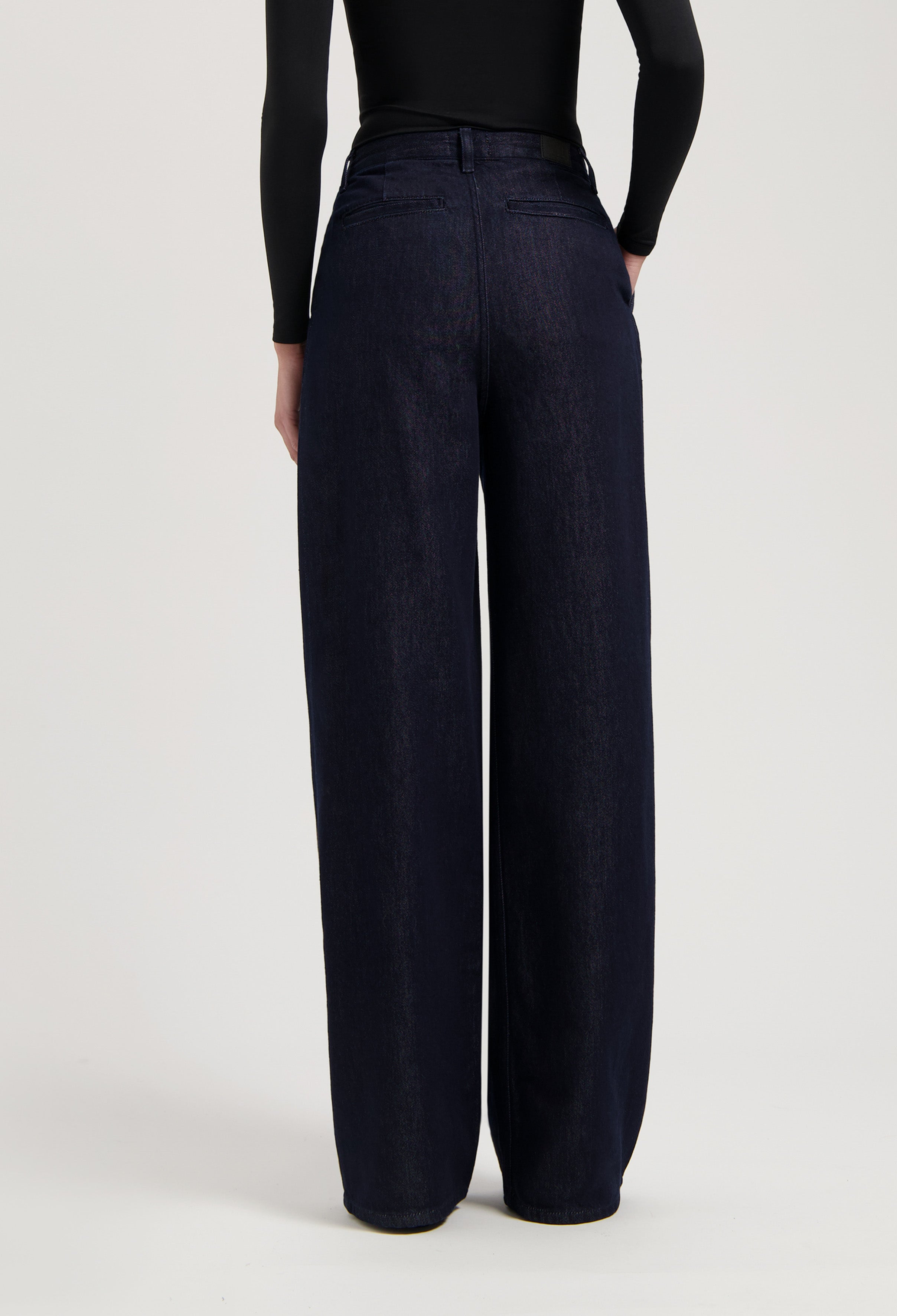 Wide-leg dark indigo denim jeans with a high waist, shown from the back, paired with a long-sleeve black top.