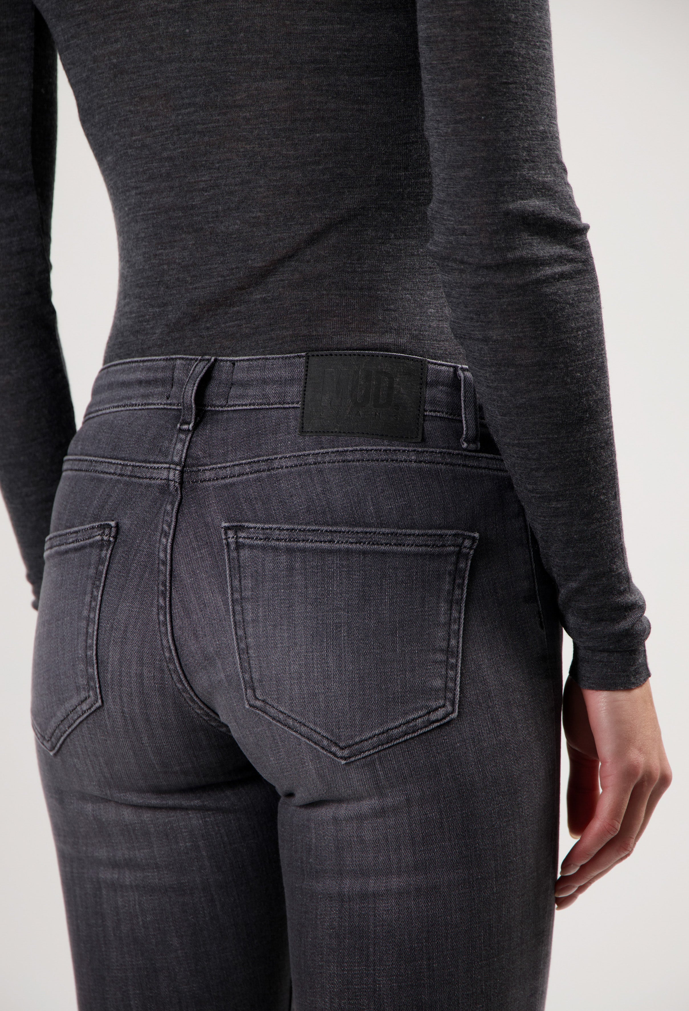 Dark gray MUD Jeans made from organic cotton, displaying a pair of slim-fit denim jeans worn with a long-sleeve gray top.