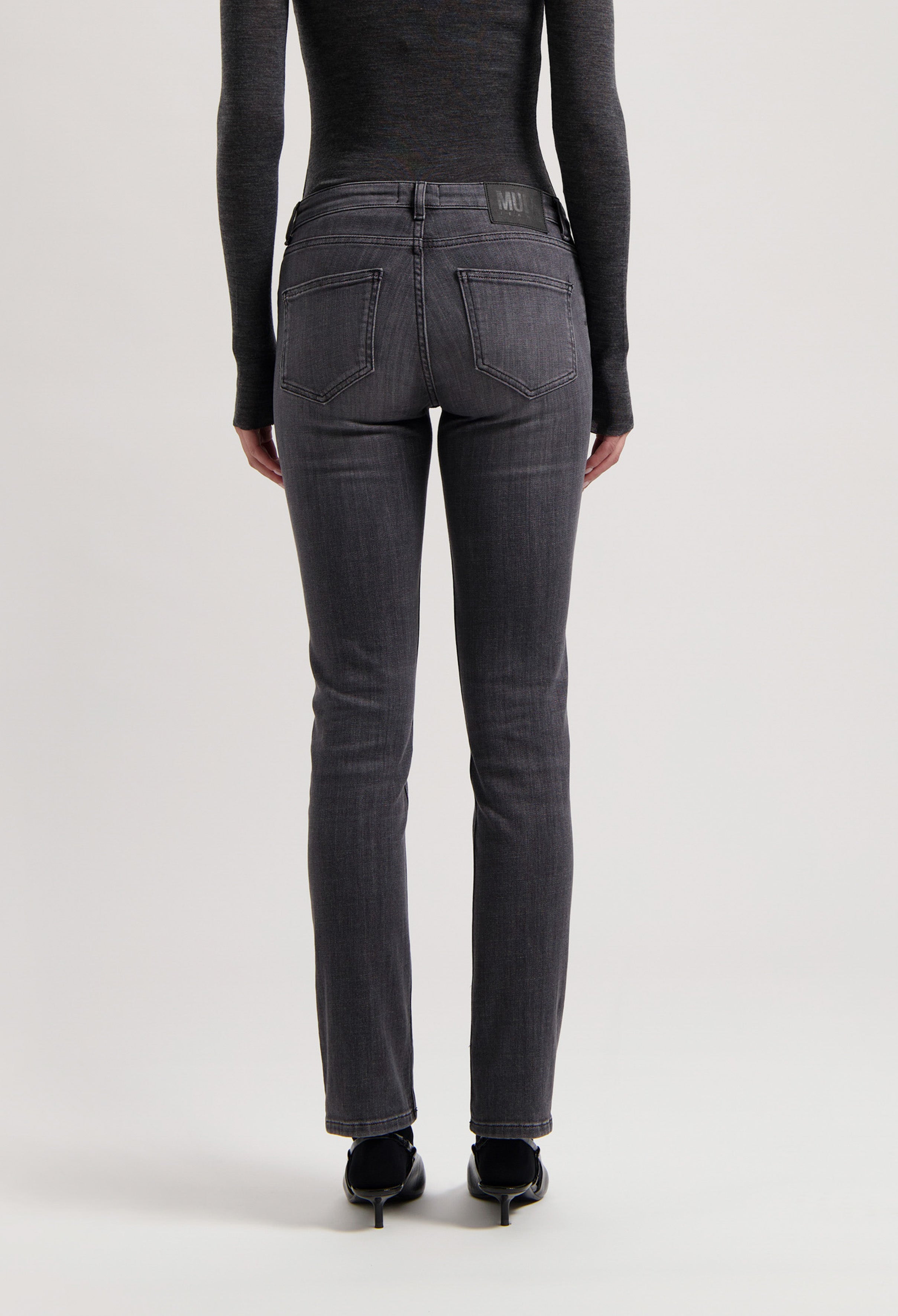 Dark gray, slim-fit MUD Jeans made from eco-friendly materials, showing a back view worn with a long-sleeve black top.
