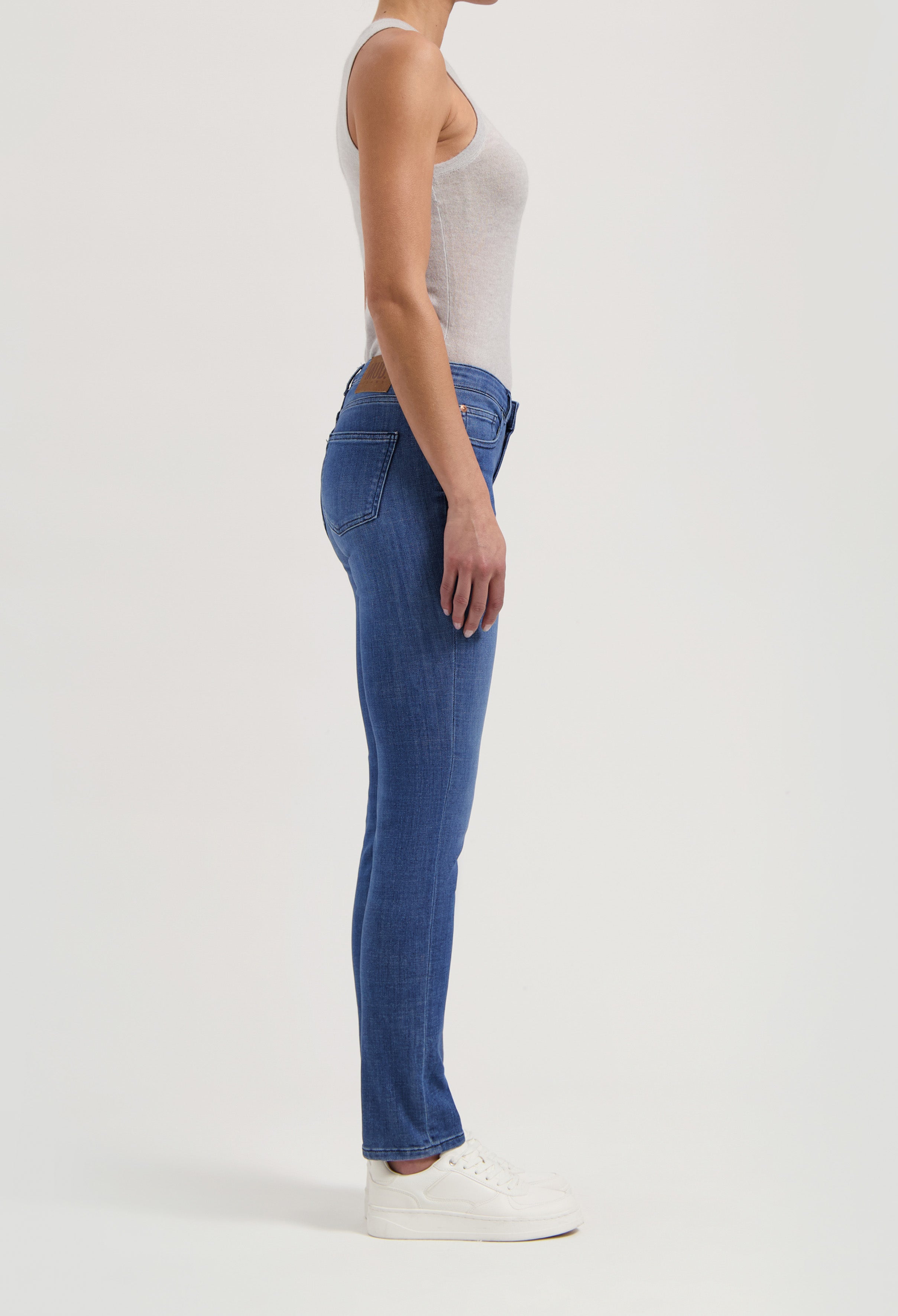 Side view of a model wearing blue slim-fit jeans paired with a light gray tank top, showcasing casual style.