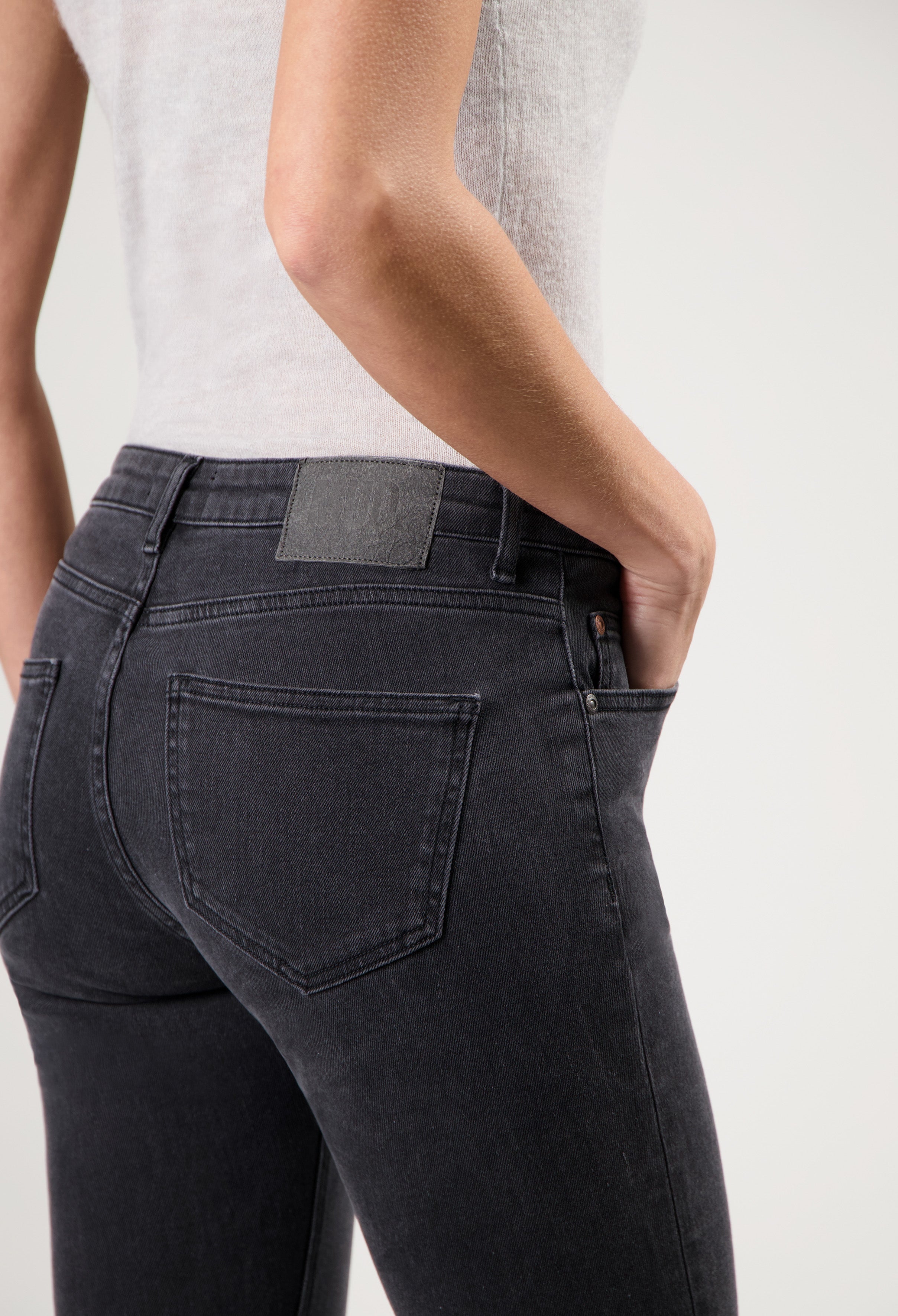 Dark charcoal slim-fit jeans, highlighting back pocket and seam detail, paired with a fitted light gray sleeveless top.