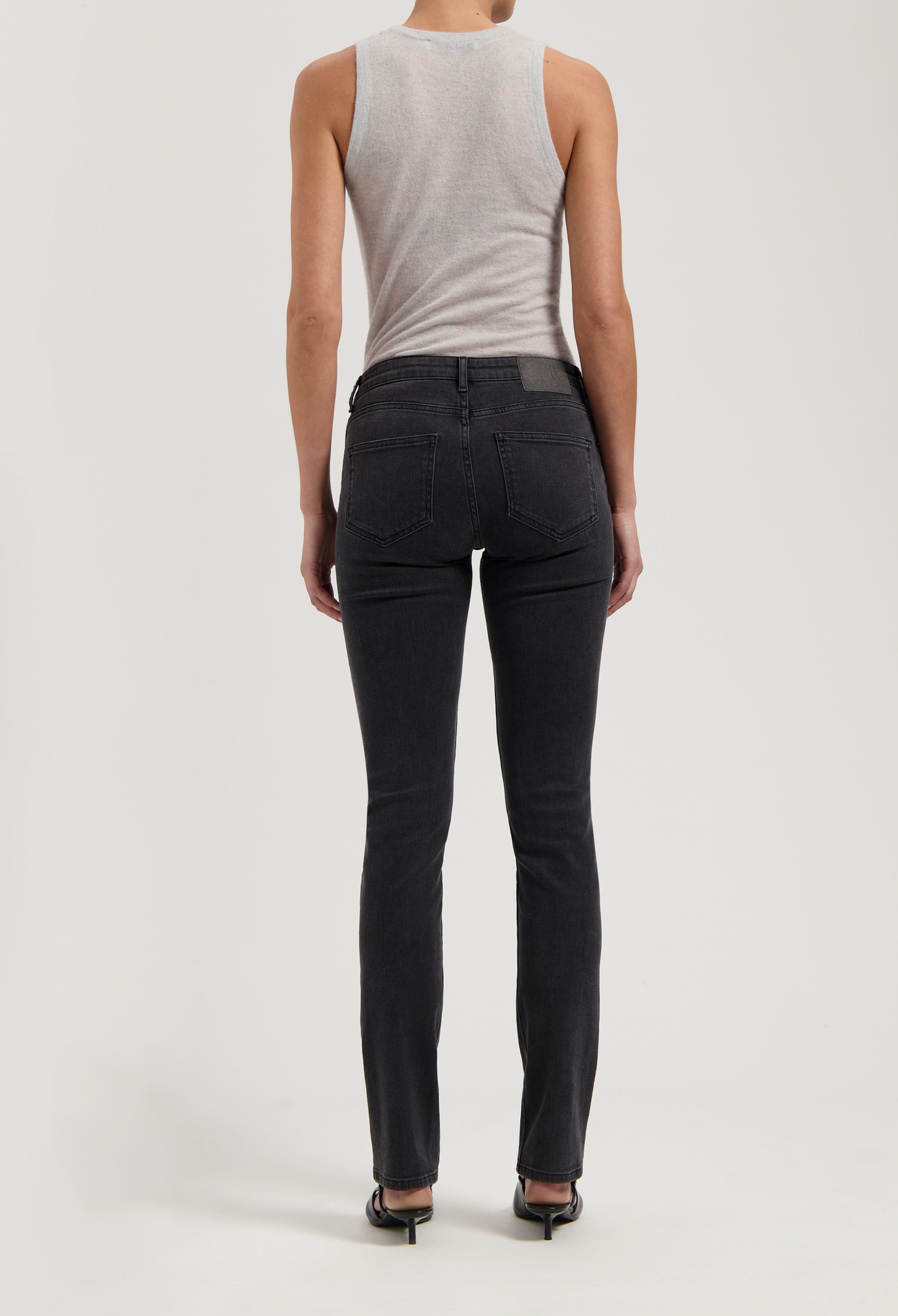 Rear view of black slim-fit denim jeans paired with a sleeveless gray top, showcased in a minimalist style.