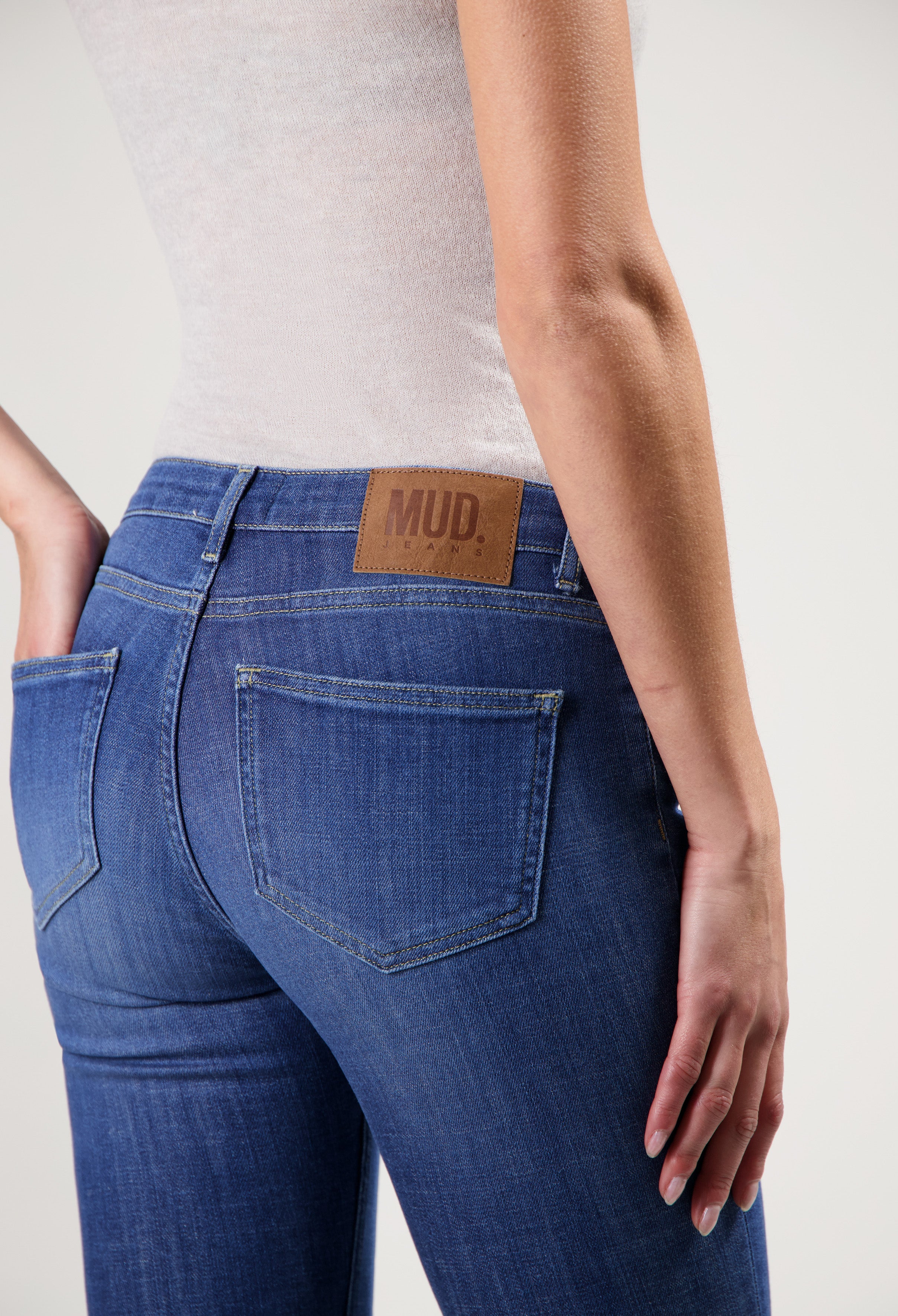 Close-up of MUD Jeans, showcasing a slim-fit design in blue denim, paired with a neutral sleeveless top.