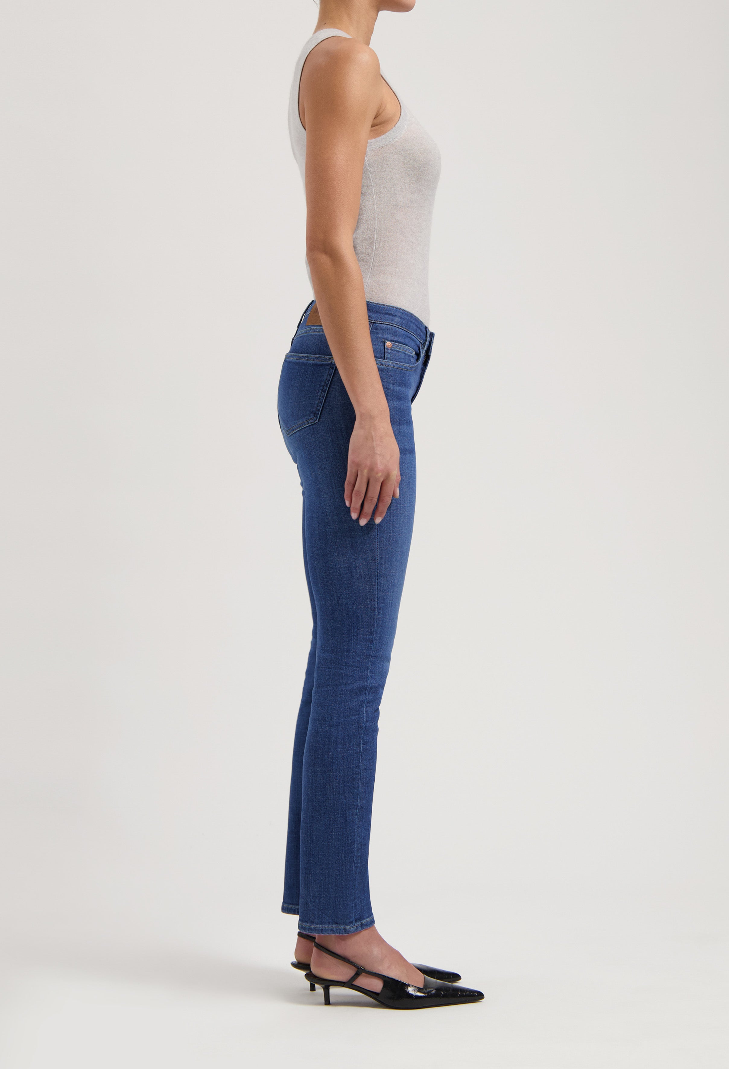 Side view of a woman wearing slim-fit blue jeans paired with a light gray tank top and black slingback heels.